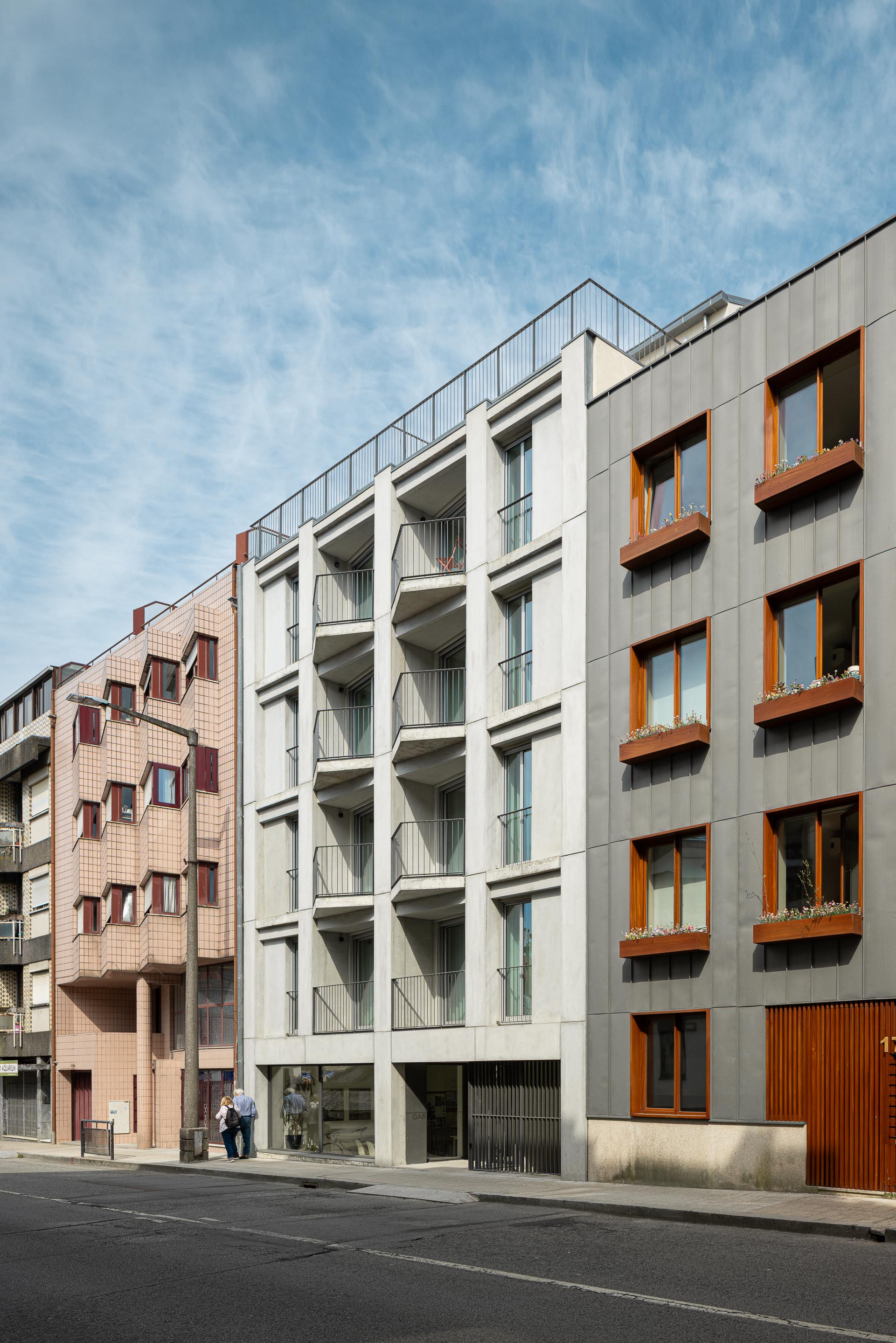 Fachada principal com painéis de betão pré-fabricado cinzento claro e varandas em betão aparente, integrando-se na malha urbana — Costa Cabral Building arquitectura ENTRETEMPOS + ATA Atelier fotografia Ivo Tavares