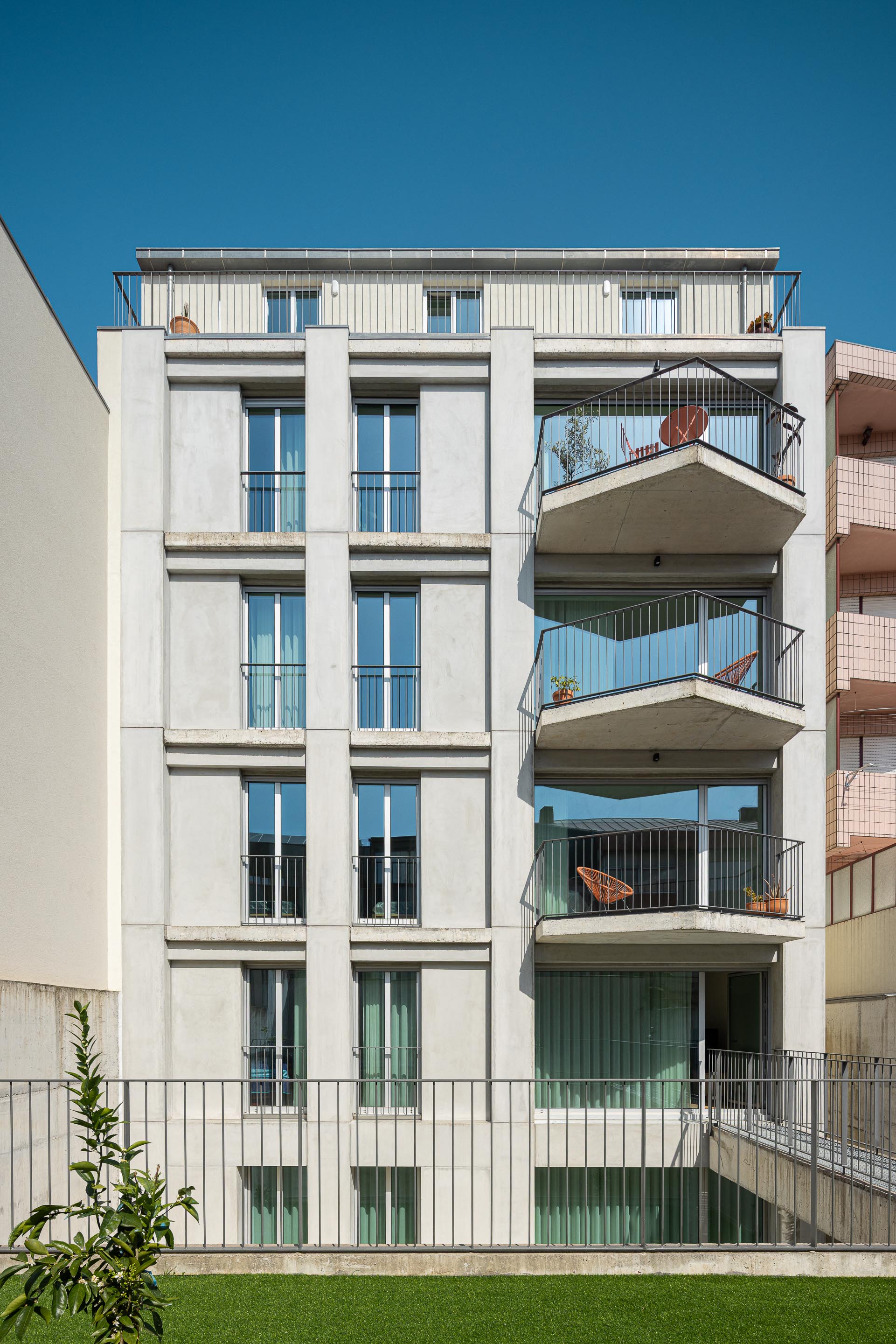 Fachada posterior em betão aparente com varandas em consola e amplos vãos, voltada para um logradouro ajardinado — Costa Cabral Building arquitectura ENTRETEMPOS + ATA Atelier fotografia Ivo Tavares