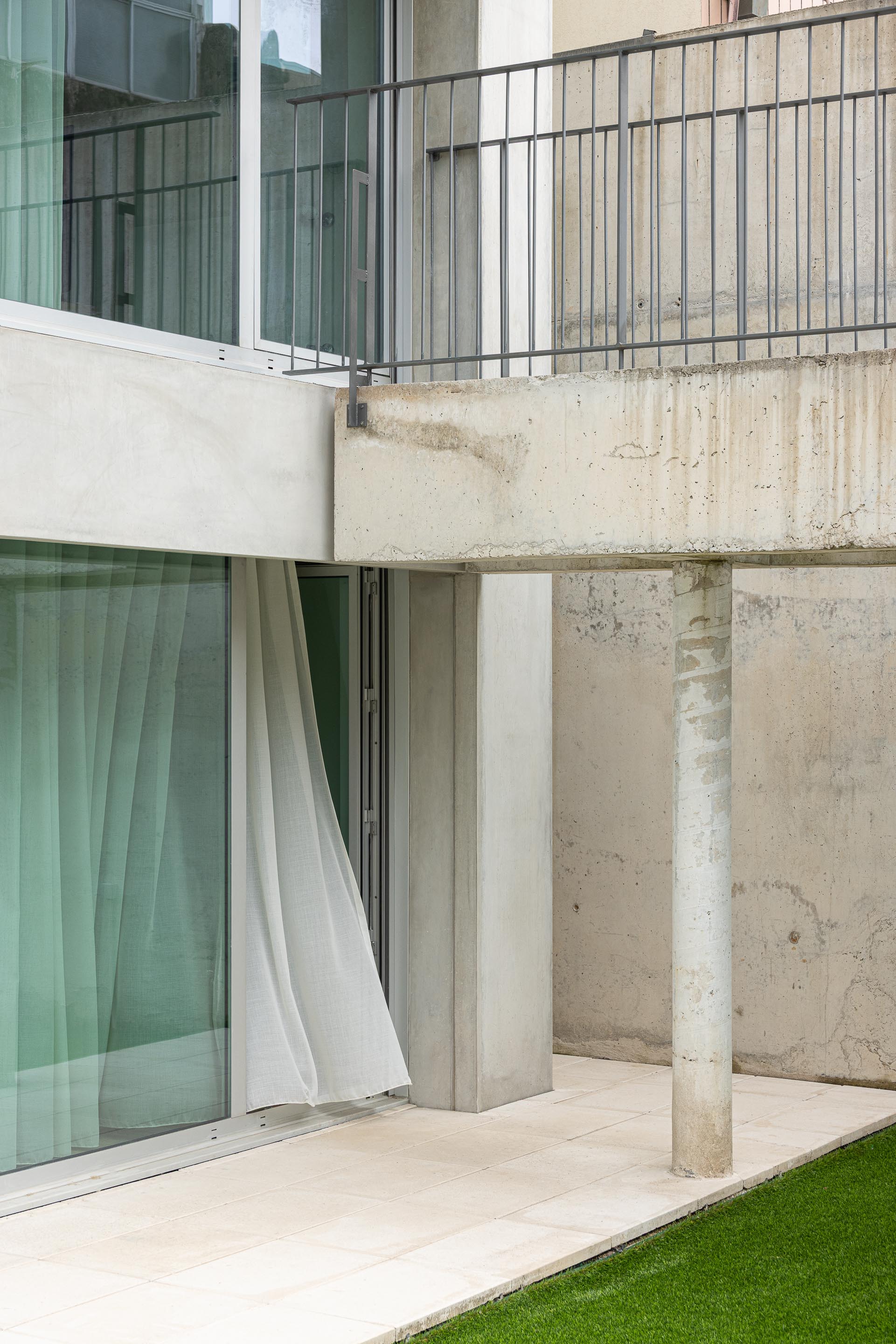 Detalhe do logradouro com pavimento em pedra clara, pilar cilíndrico de betão aparente e varanda em consola — Costa Cabral Building arquitectura ENTRETEMPOS + ATA Atelier fotografia Ivo Tavares