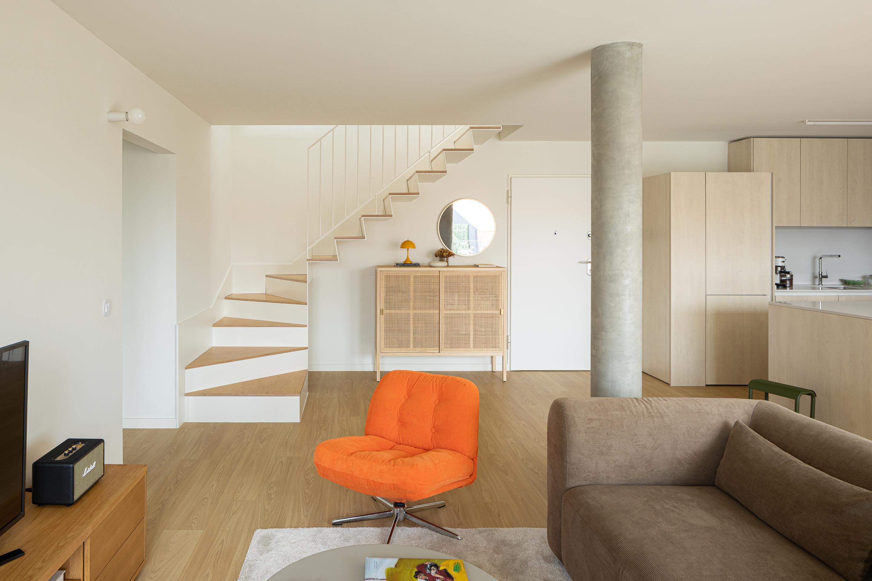 Sala de estar com pavimento em madeira clara, paredes brancas e pilar cilíndrico de betão aparente, integrada com escada — Costa Cabral Building arquitectura ENTRETEMPOS + ATA Atelier fotografia Ivo Tavares