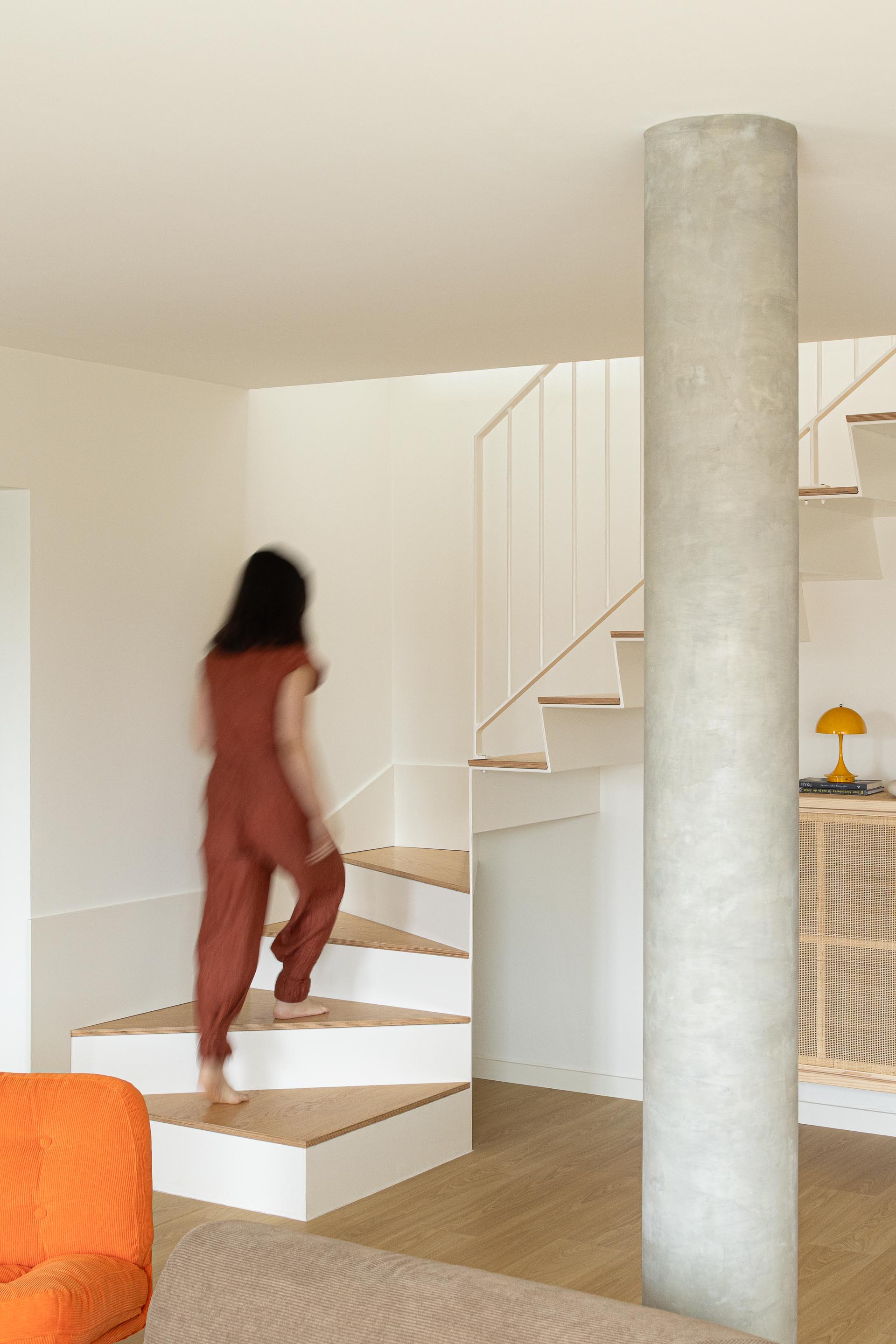 Perspetiva da sala de estar com pavimento em madeira clara, pilar cilíndrico de betão aparente e escada de acesso ao piso superior — Costa Cabral Building arquitectura ENTRETEMPOS + ATA Atelier fotografia Ivo Tavares
