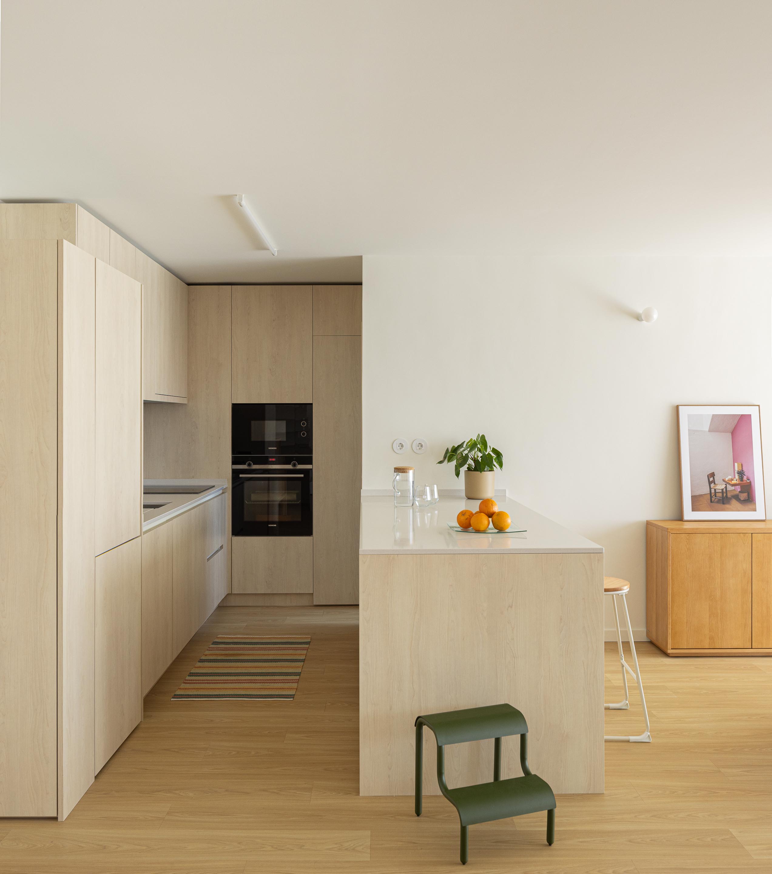 Cozinha com armários em madeira clara e bancada branca, integrada na área social com pavimento em madeira clara — Costa Cabral Building arquitectura ENTRETEMPOS + ATA Atelier fotografia Ivo Tavares