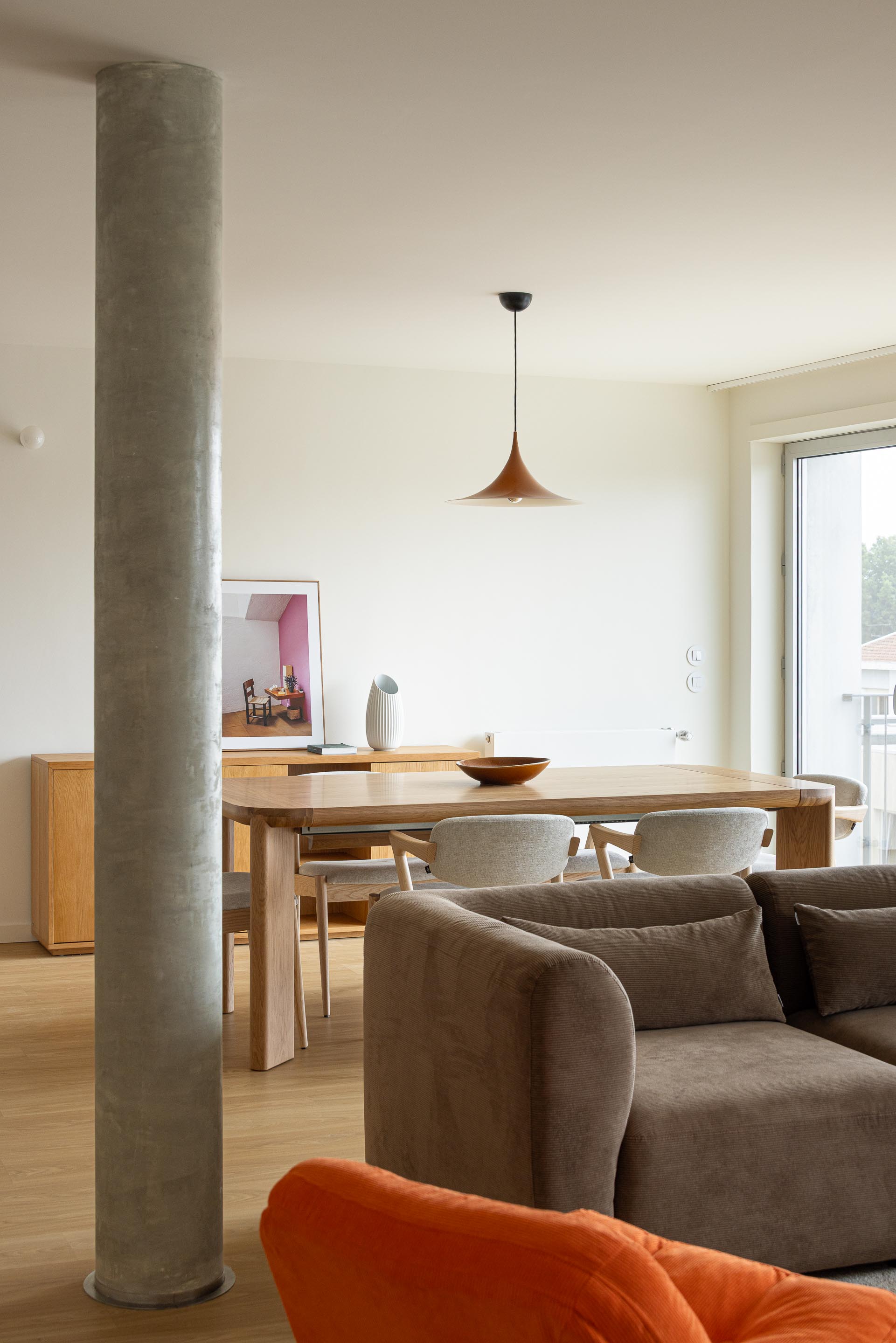 Sala de jantar com mesa e cadeiras em madeira, pavimento em madeira clara e pilar cilíndrico de betão aparente — Costa Cabral Building arquitectura ENTRETEMPOS + ATA Atelier fotografia Ivo Tavares