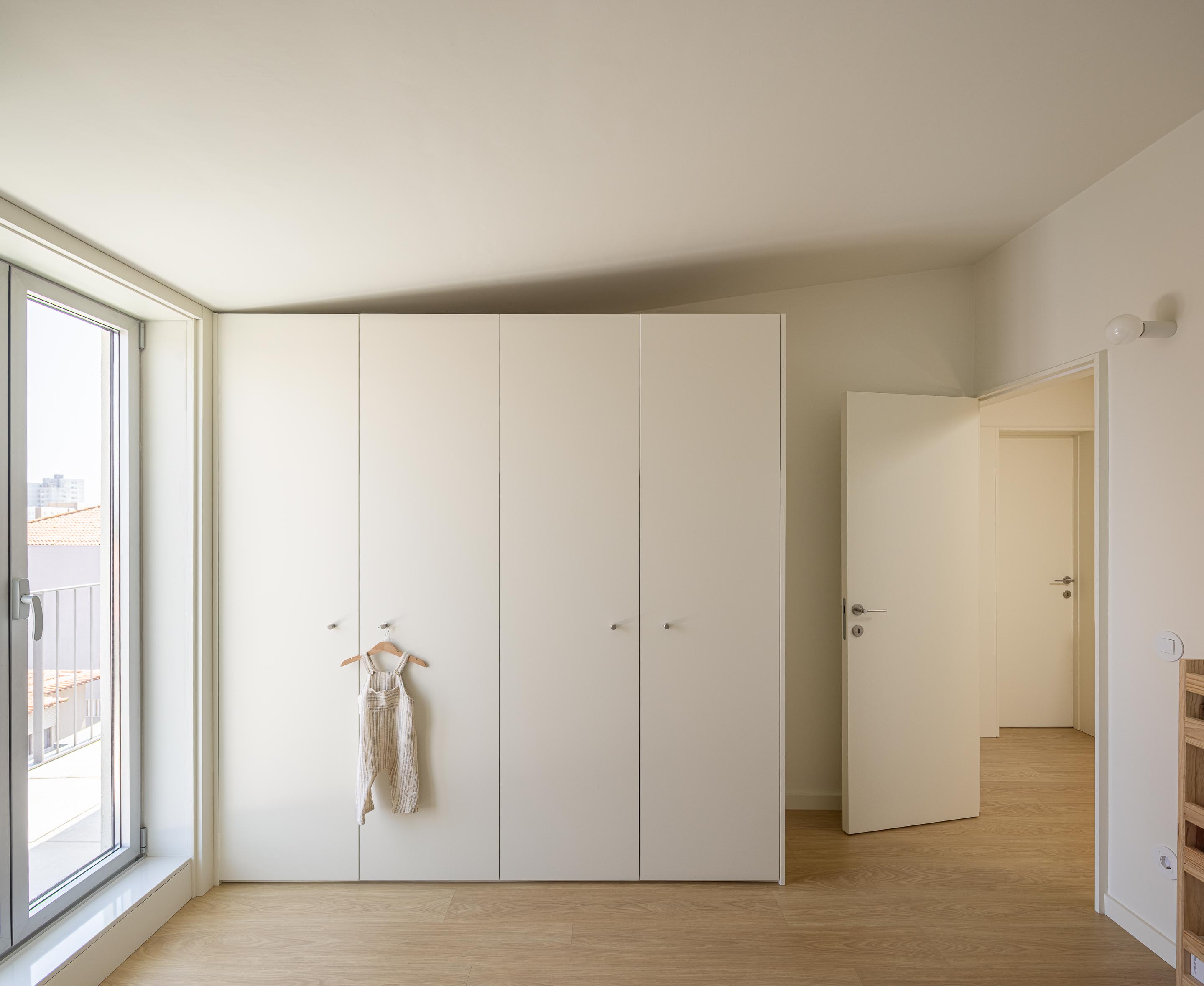 Quarto com pavimento em madeira clara, roupeiro embutido branco e acesso a varanda através de amplo vão — Costa Cabral Building arquitectura ENTRETEMPOS + ATA Atelier fotografia Ivo Tavares
