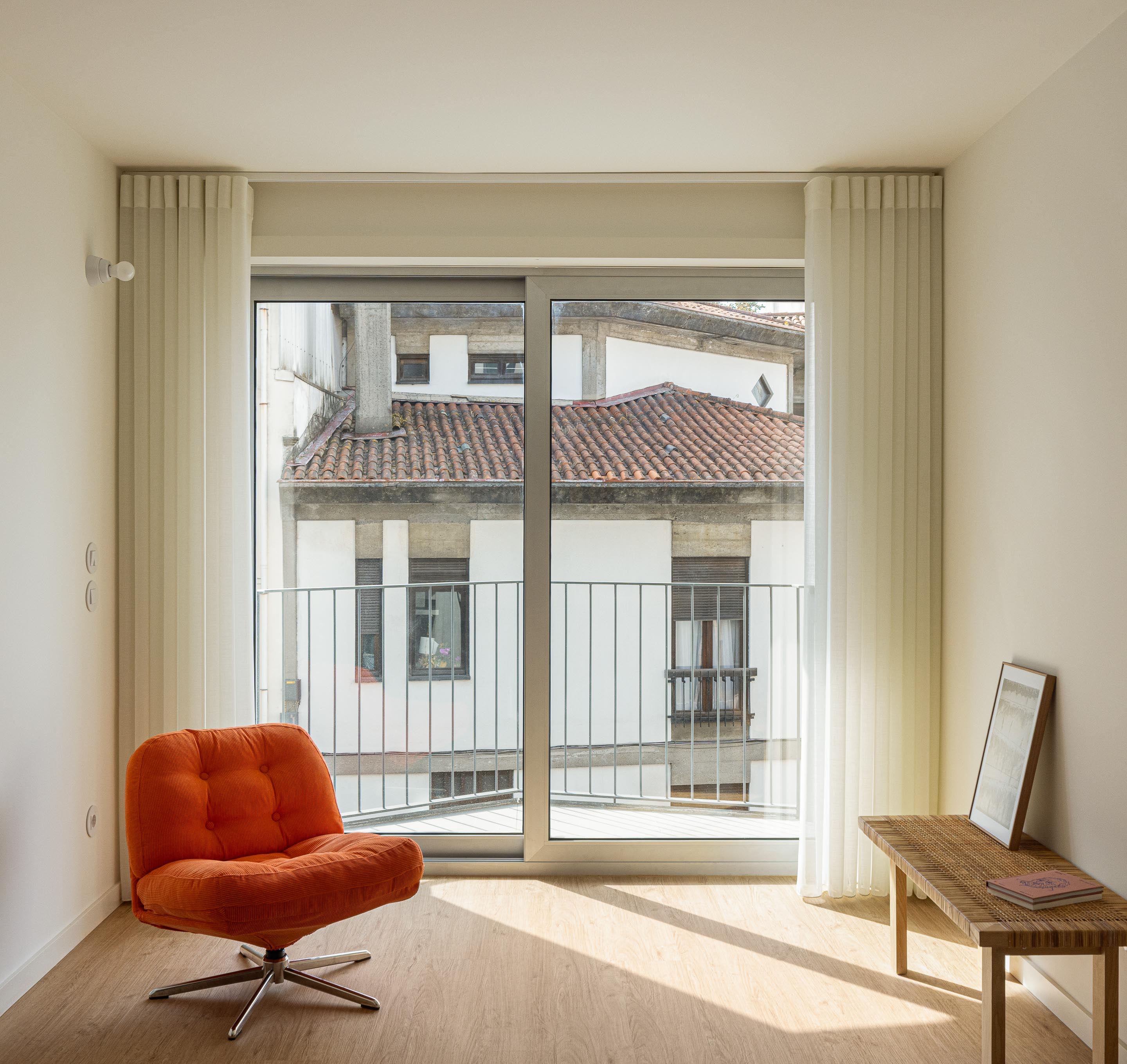 Quarto com pavimento em madeira clara e amplo vão de varanda, oferecendo vista para o contexto urbano — Costa Cabral Building arquitectura ENTRETEMPOS + ATA Atelier fotografia Ivo Tavares