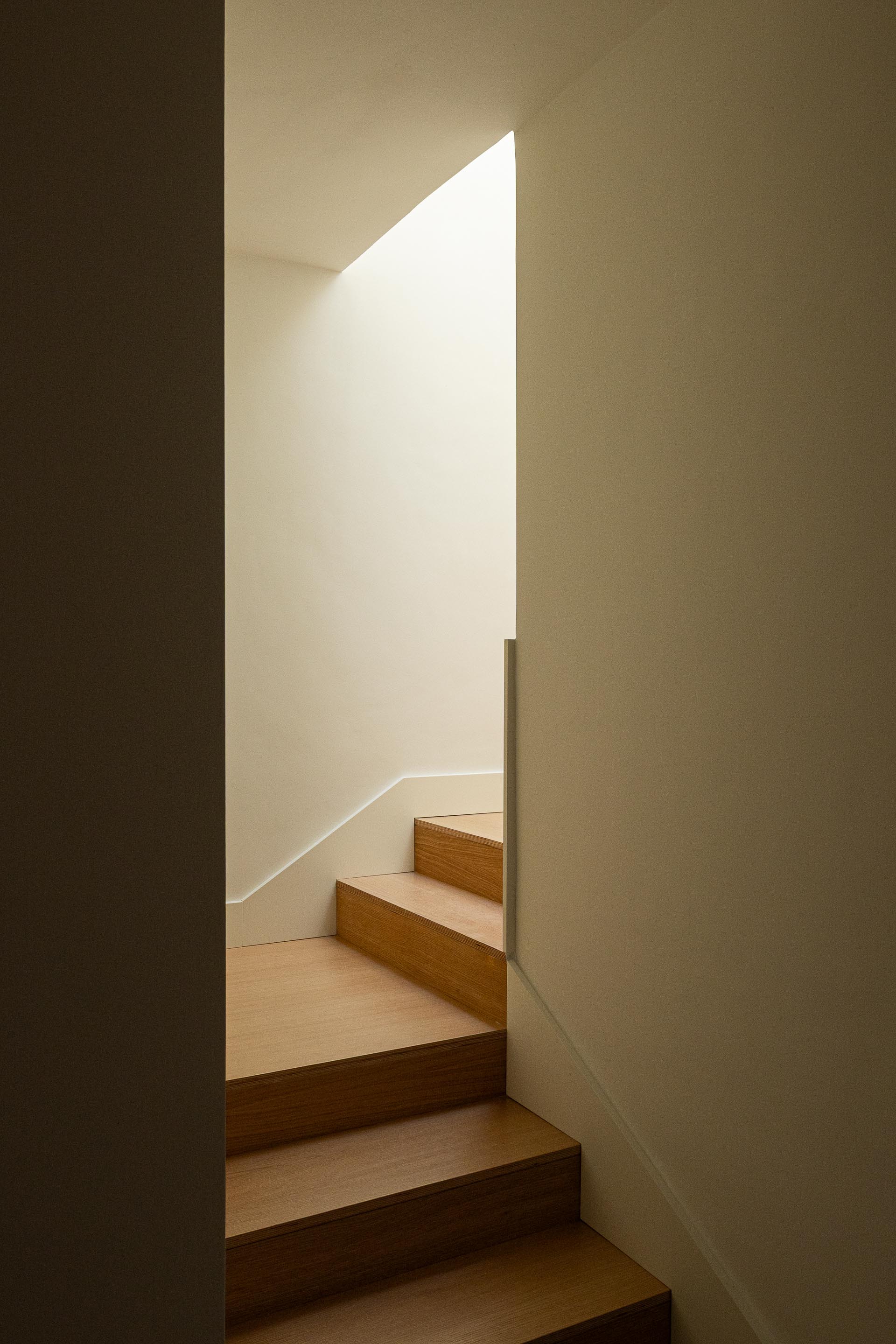 Escada com degraus em madeira clara, iluminada por luz zenital que realça a verticalidade do espaço — Costa Cabral Building arquitectura ENTRETEMPOS + ATA Atelier fotografia Ivo Tavares
