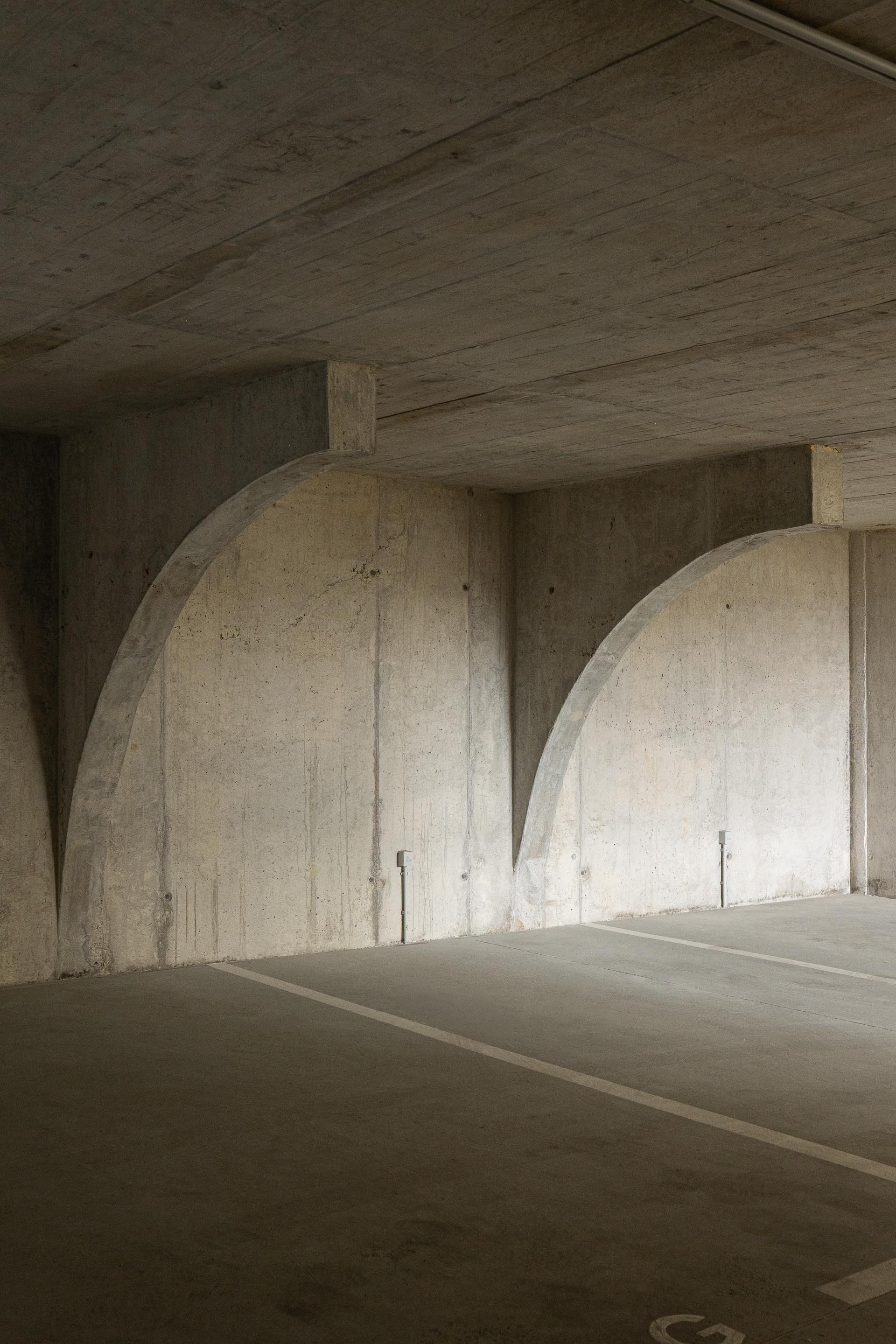 Garagem subterrânea em betão aparente cinzento, com arcos estruturais que conferem ritmo e robustez ao espaço — Costa Cabral Building arquitectura ENTRETEMPOS + ATA Atelier fotografia Ivo Tavares