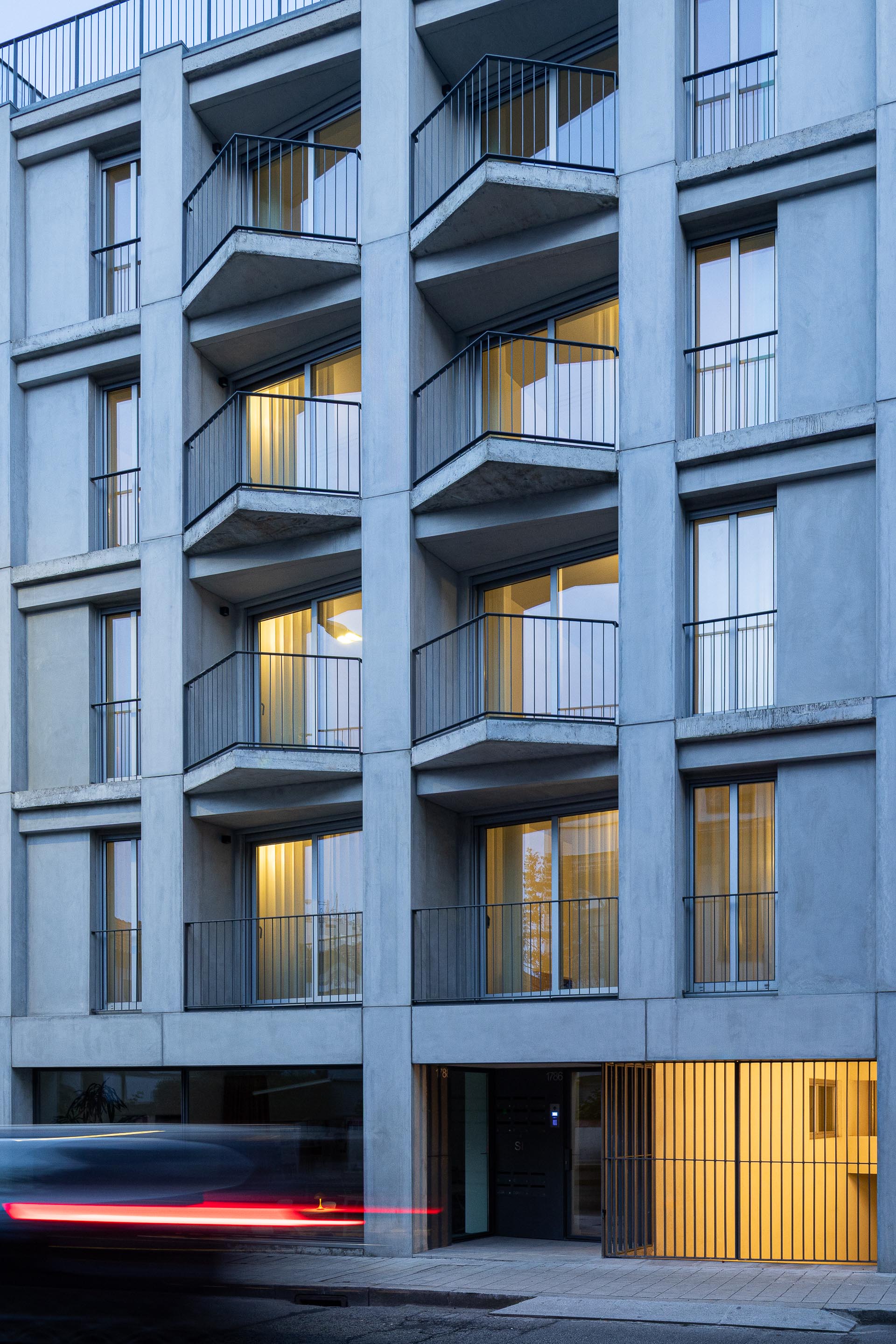 Fachada principal à noite, com varandas em betão aparente e vãos iluminados, destacando a composição volumétrica — Costa Cabral Building arquitectura ENTRETEMPOS + ATA Atelier fotografia Ivo Tavares