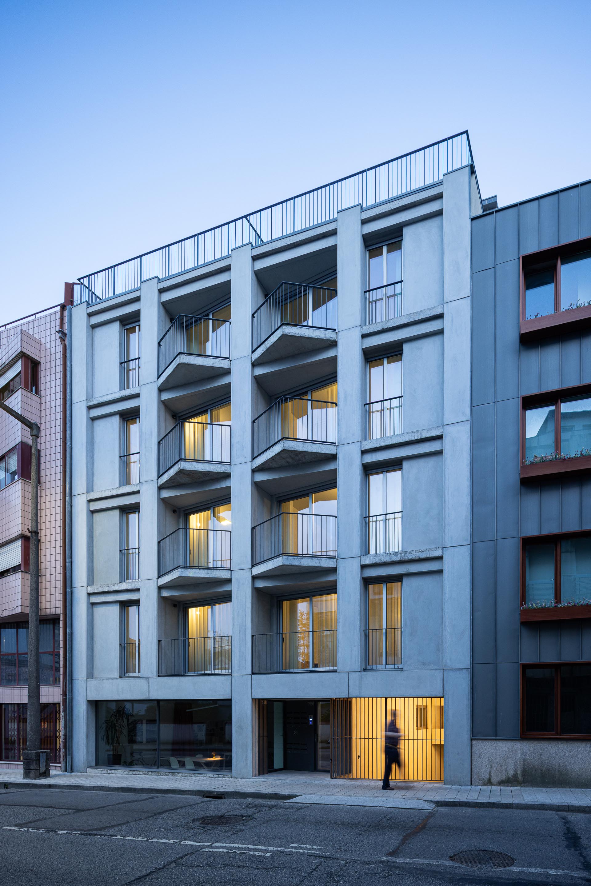 Fachada principal ao crepúsculo, com a iluminação interior a realçar a volumetria em betão e as varandas salientes — Costa Cabral Building arquitectura ENTRETEMPOS + ATA Atelier fotografia Ivo Tavares