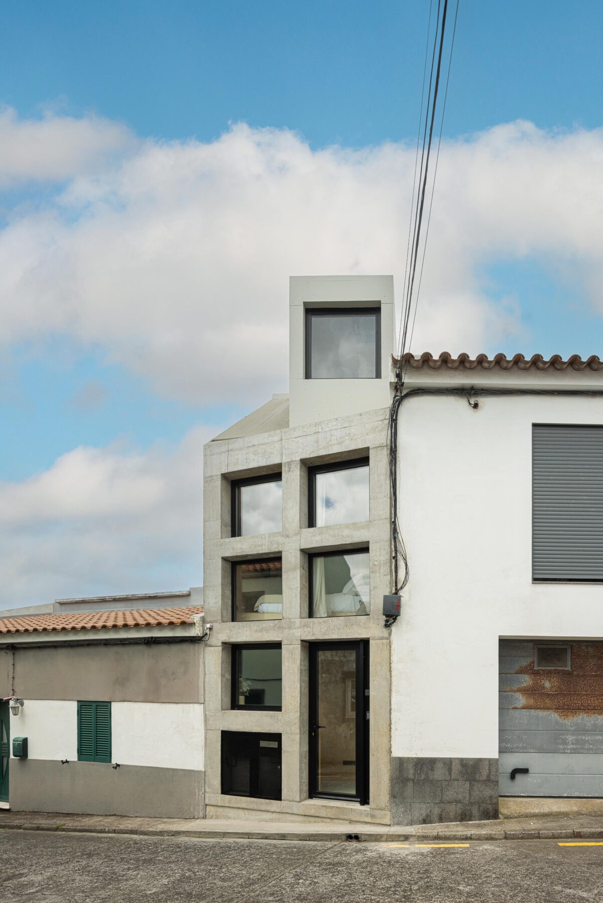 Fachada em betão aparente cinzento com vãos quadrados e torre superior, integrada na frente urbana — MINI ATALHADA arquitectura SO Arquitetura & Design fotografia Ivo Tavares