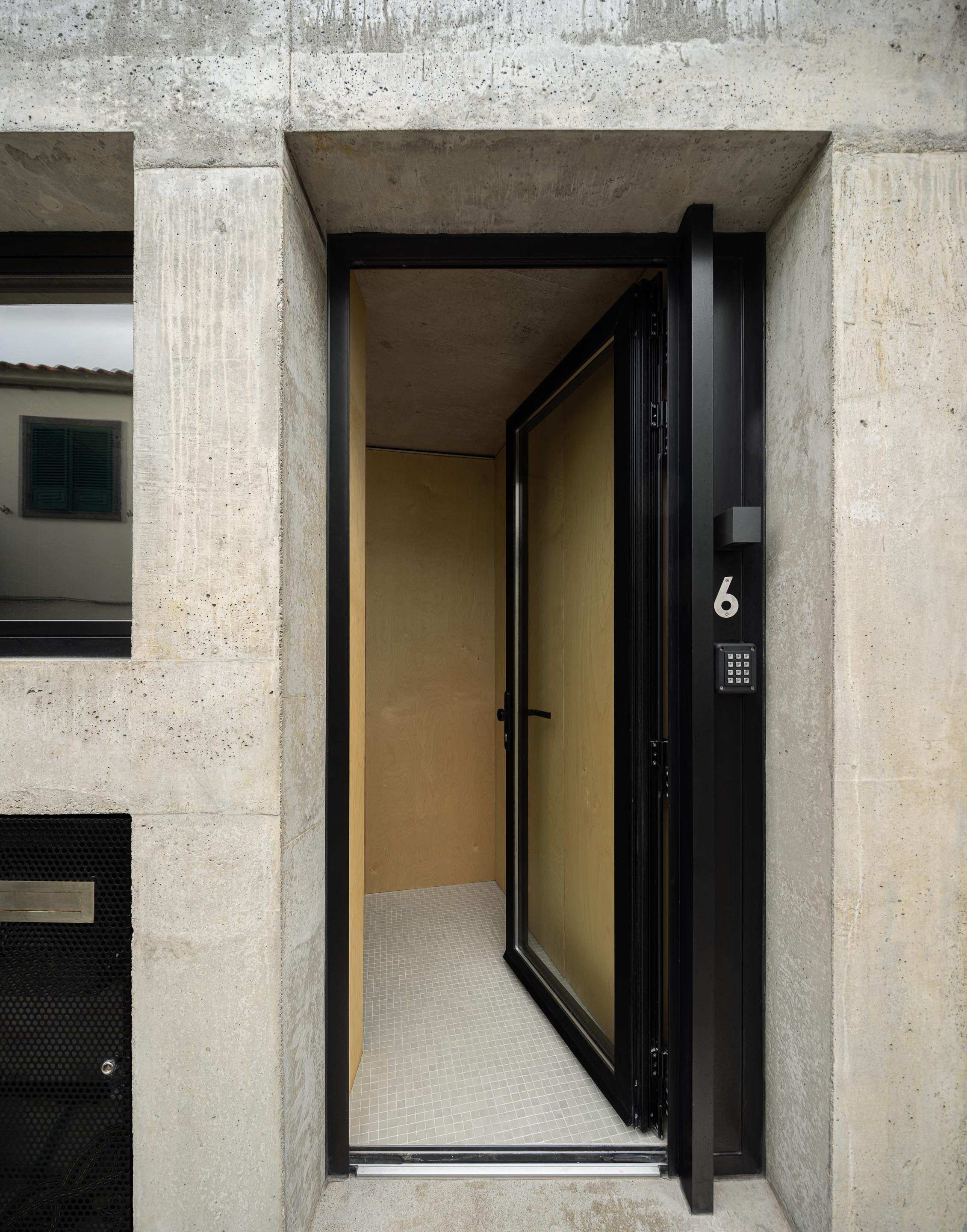 Entrada da moradia com porta preta envidraçada, pavimento em mosaico branco e paredes em betão aparente e madeira clara — MINI ATALHADA arquitectura SO Arquitetura & Design fotografia Ivo Tavares
