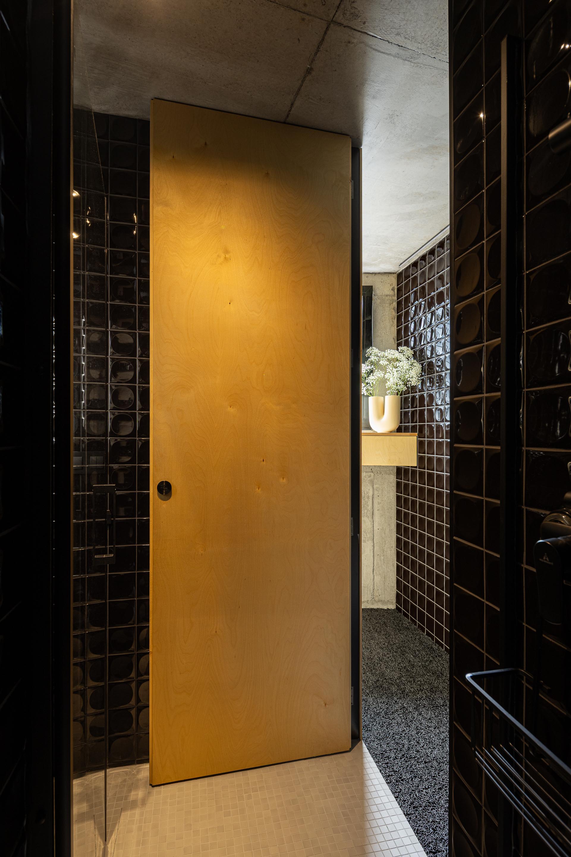 Casa de banho com paredes em azulejo preto brilhante, pavimento em mosaico branco e porta em madeira clara — MINI ATALHADA arquitectura SO Arquitetura & Design fotografia Ivo Tavares