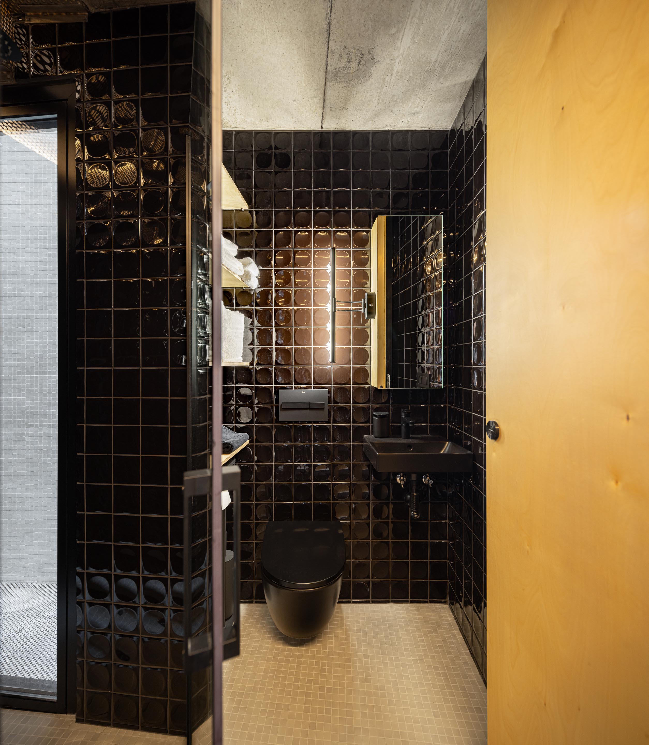 Casa de banho com paredes em azulejo preto brilhante, sanita e lavatório pretos, e espelho iluminado — MINI ATALHADA arquitectura SO Arquitetura & Design fotografia Ivo Tavares