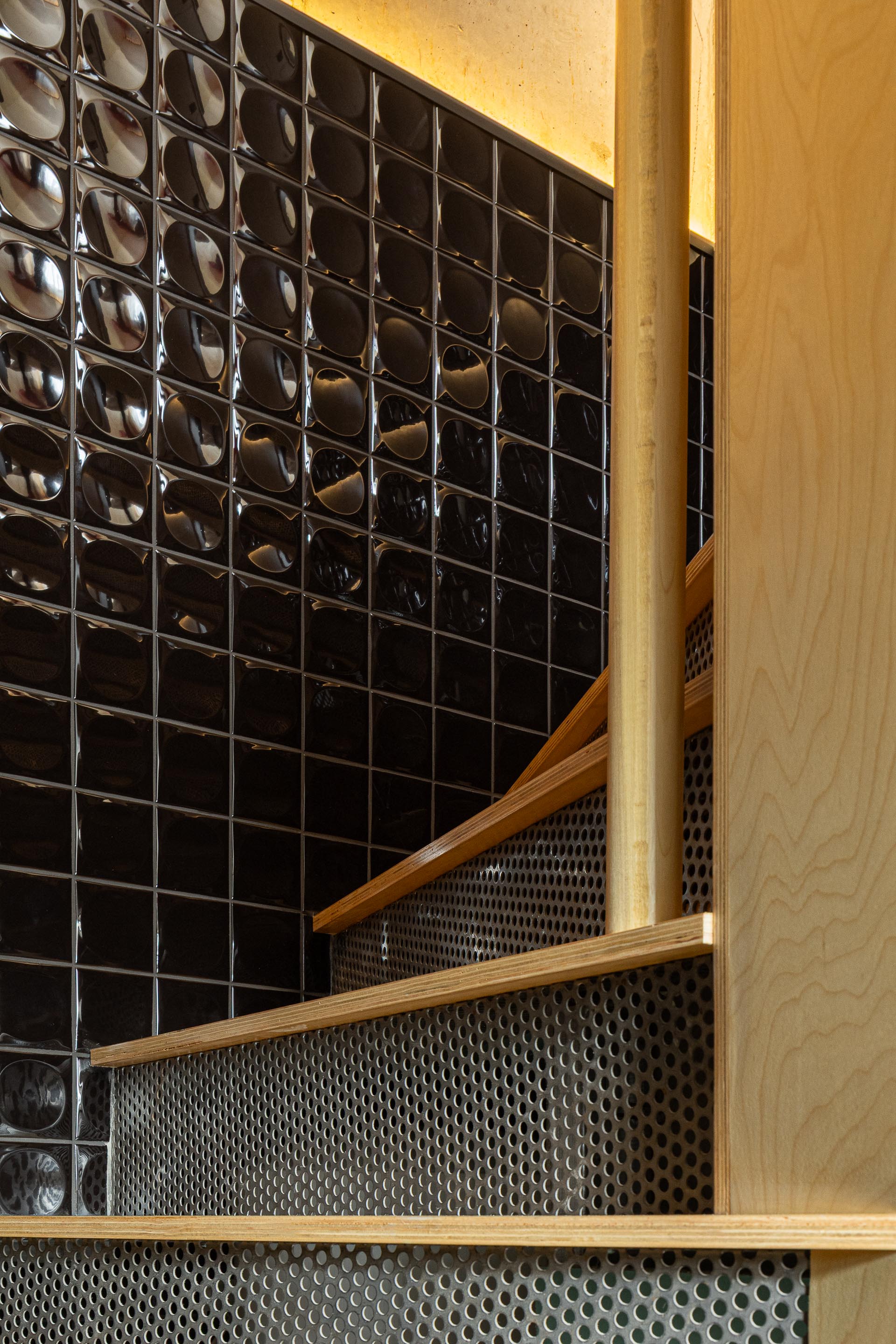 Detalhe da escada em chapa metálica perfurada e madeira clara, junto a parede de azulejo preto — MINI ATALHADA arquitectura SO Arquitetura & Design fotografia Ivo Tavares