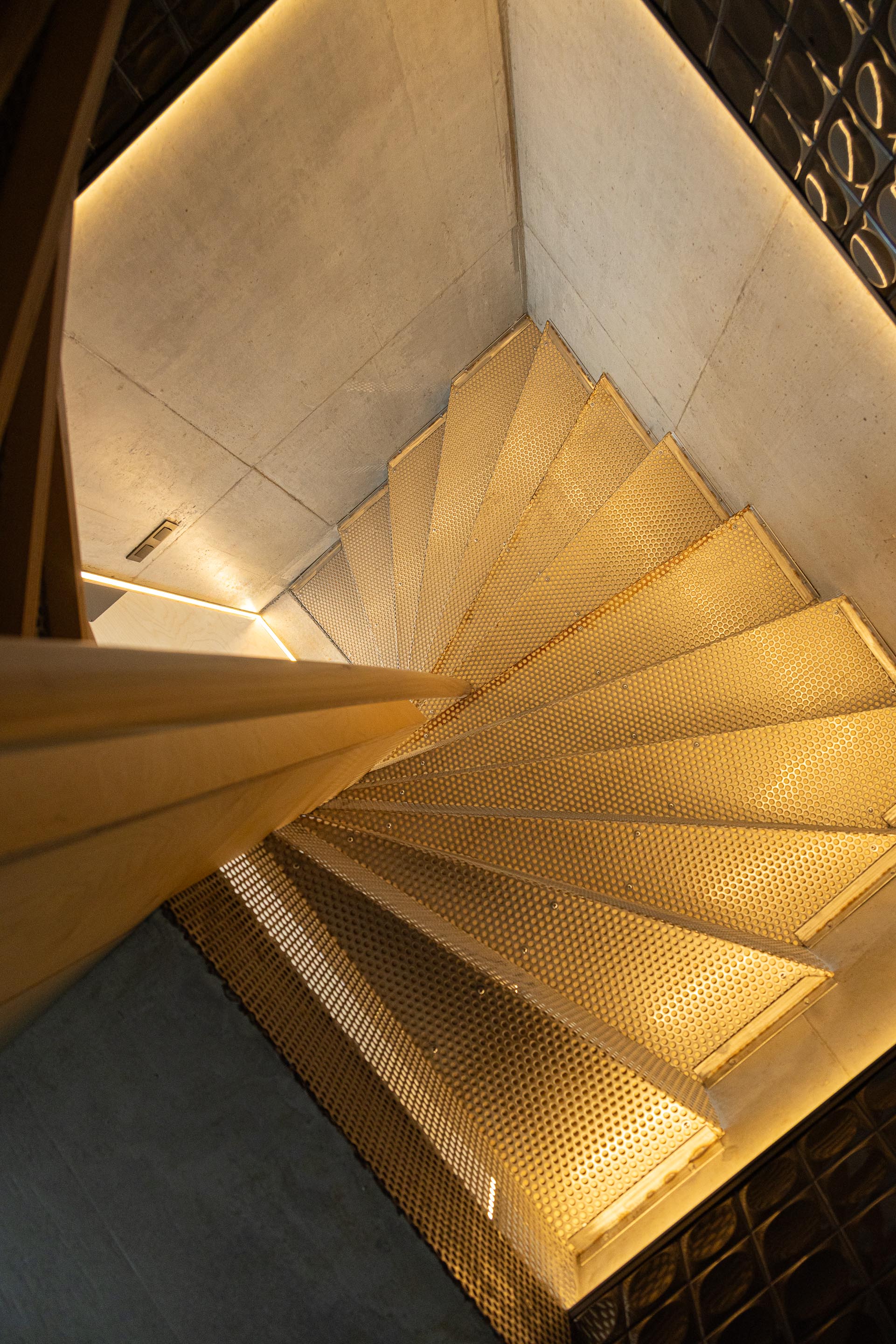 Escada em espiral com degraus em chapa metálica perfurada e madeira, iluminada por luz integrada — MINI ATALHADA arquitectura SO Arquitetura & Design fotografia Ivo Tavares