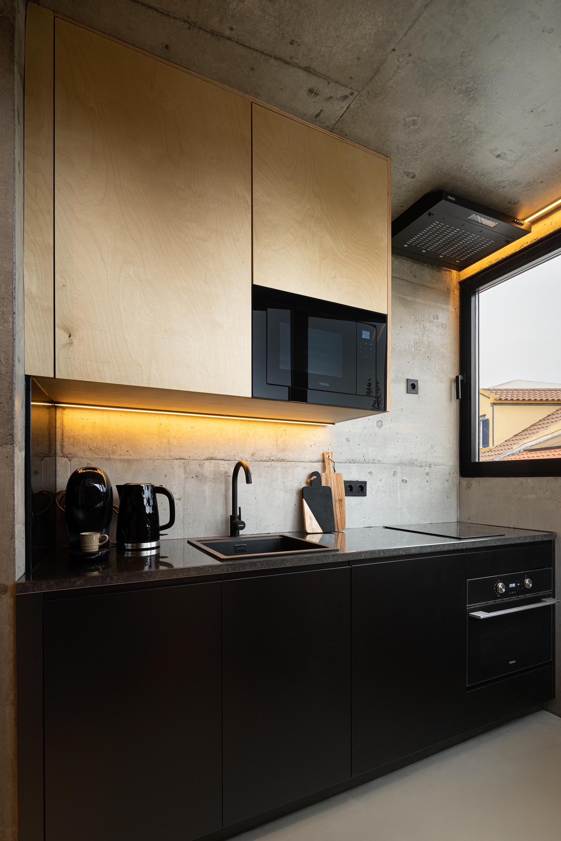 Cozinha com bancada em pedra negra, armários em madeira clara e betão aparente, e iluminação linear — MINI ATALHADA arquitectura SO Arquitetura & Design fotografia Ivo Tavares
