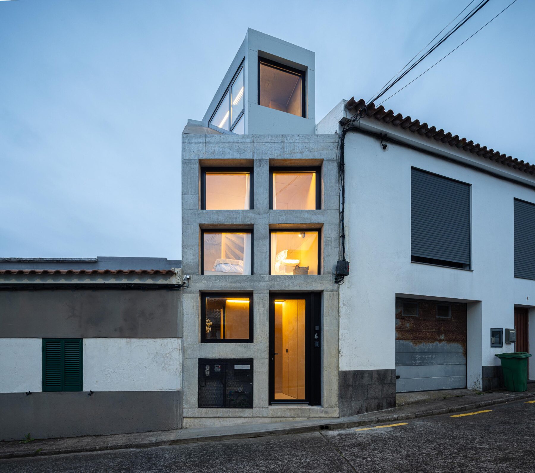 Fachada em betão aparente cinzento à noite, com iluminação interior visível através dos vãos — MINI ATALHADA arquitectura SO Arquitetura & Design fotografia Ivo Tavares