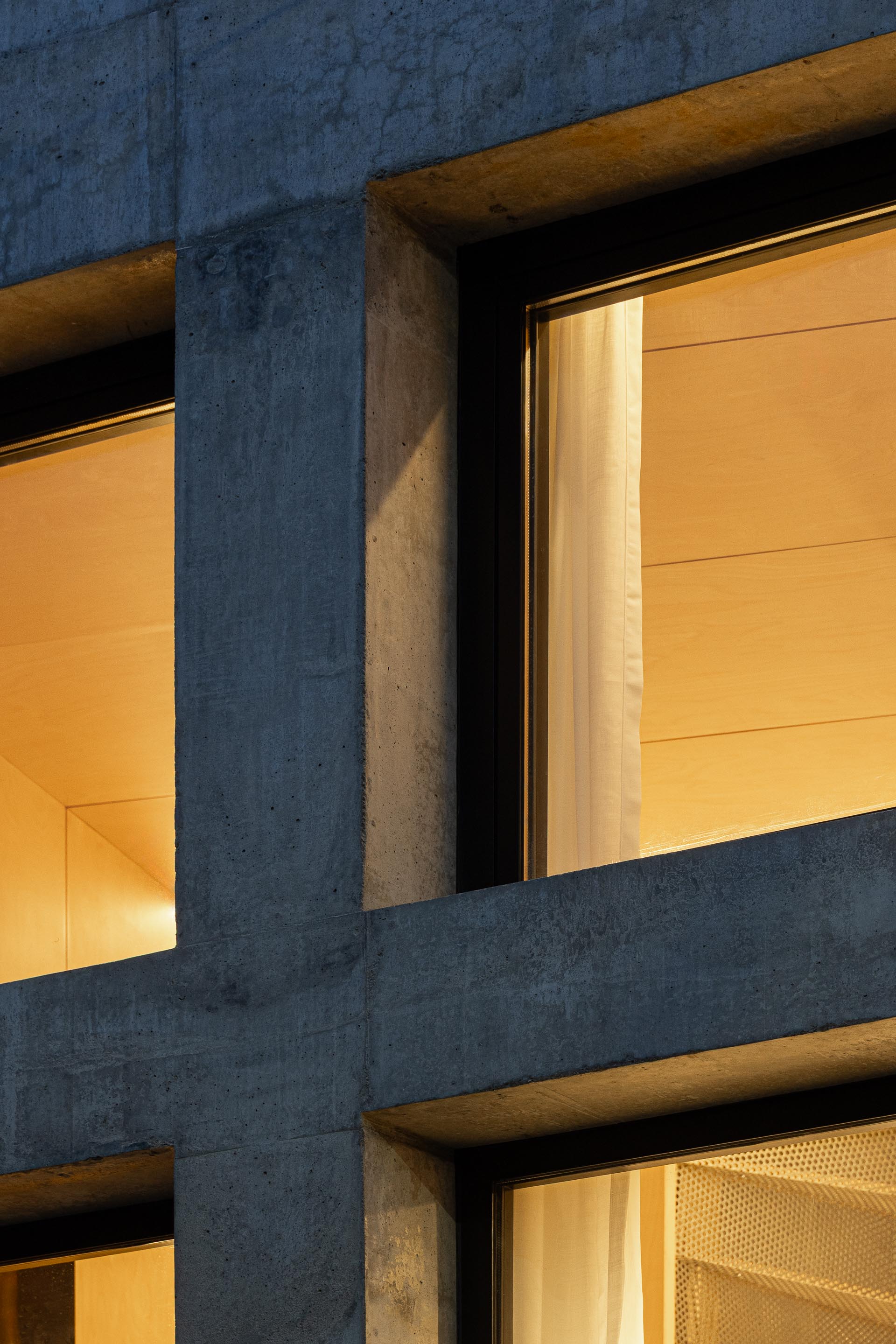 Detalhe da fachada em betão aparente com caixilharia preta, revelando interior em madeira clara iluminado — MINI ATALHADA arquitectura SO Arquitetura & Design fotografia Ivo Tavares