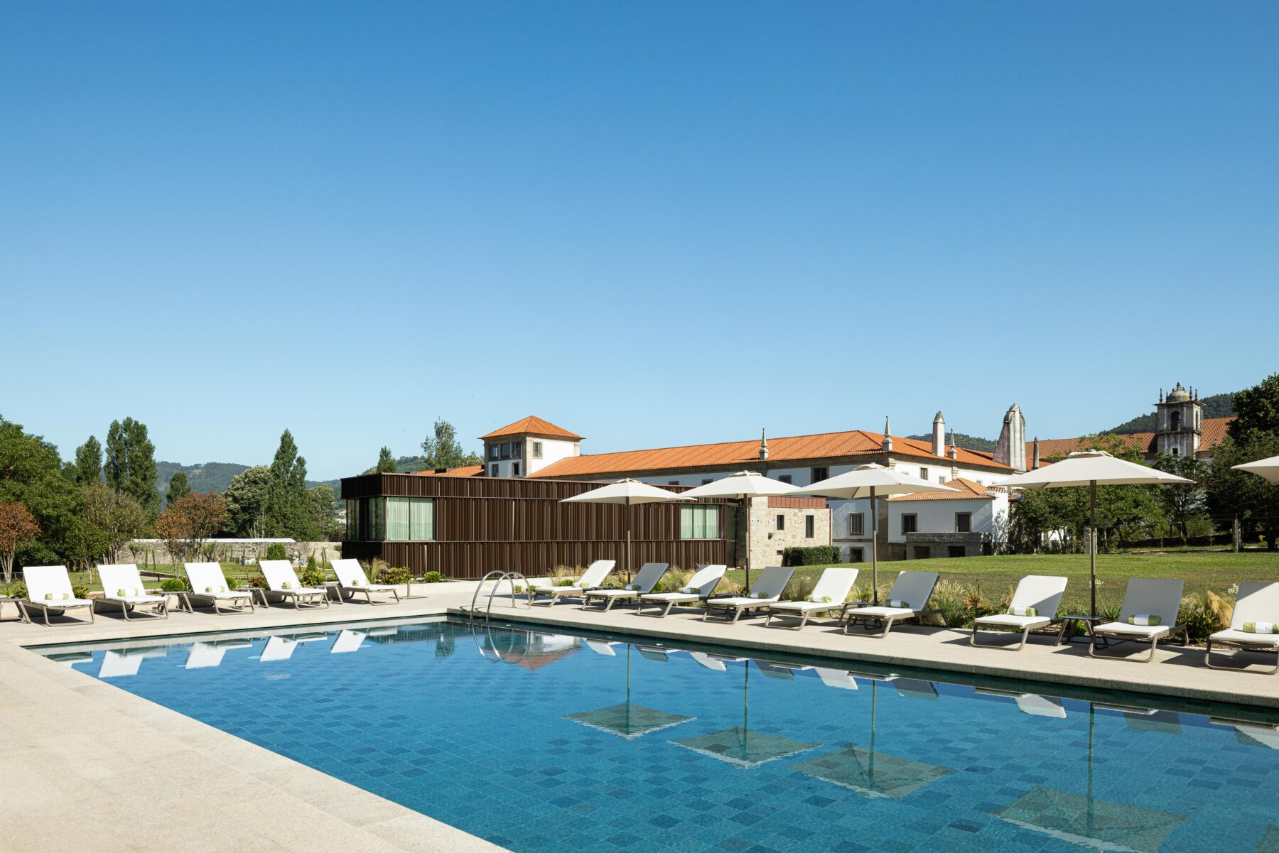 Piscina exterior com pavimento em pedra clara, ladeada por espreguiçadeiras e o edifício histórico ao fundo — MS COLLECTION AROUCA arquitectura MIMOOL ARQUITECTURA & INTERIORES fotografia Ivo Tavares