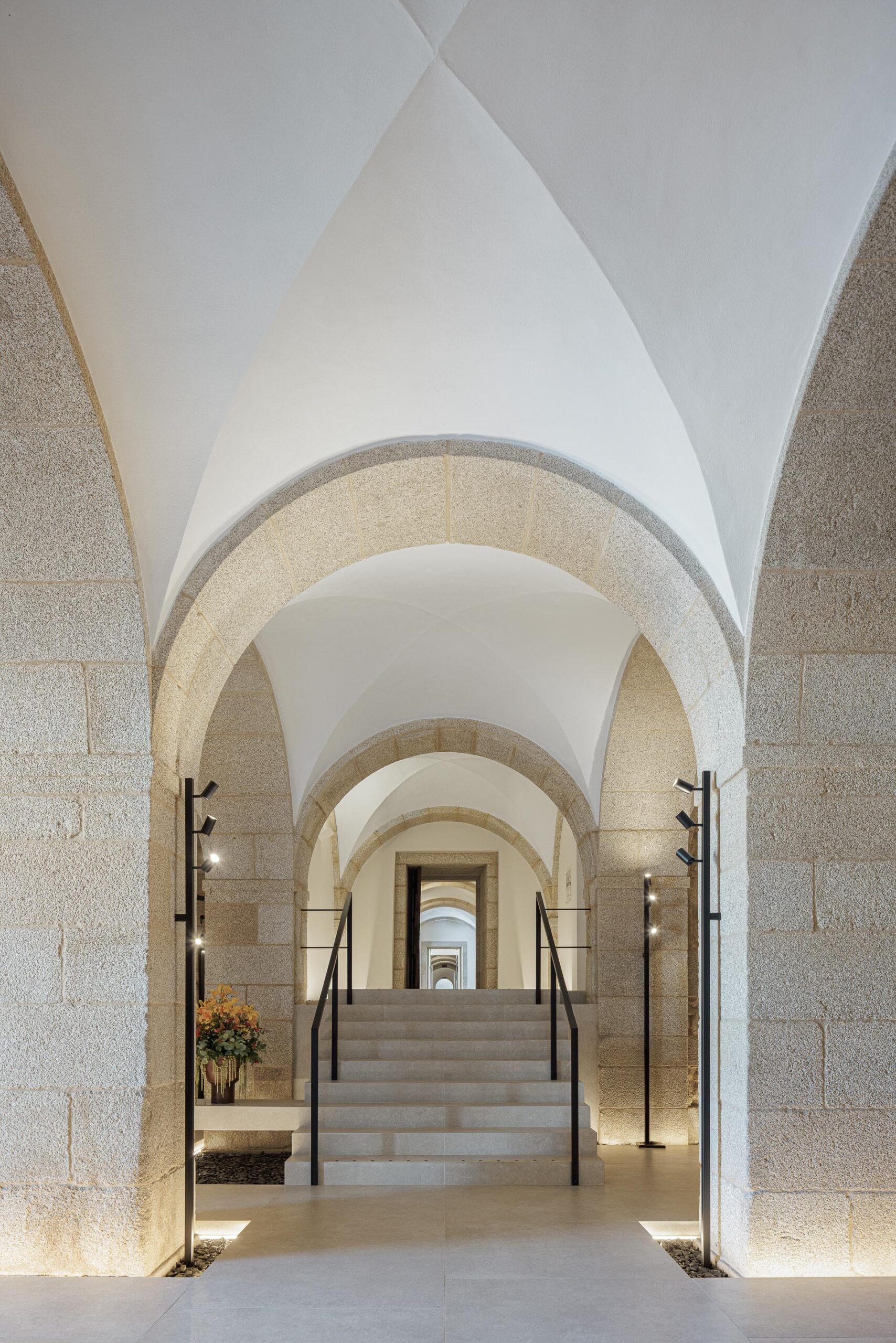 Escadaria em pedra clara no interior do hall, com arcos e abóbadas de pedra e iluminação subtil — MS COLLECTION AROUCA arquitectura MIMOOL ARQUITECTURA & INTERIORES fotografia Ivo Tavares