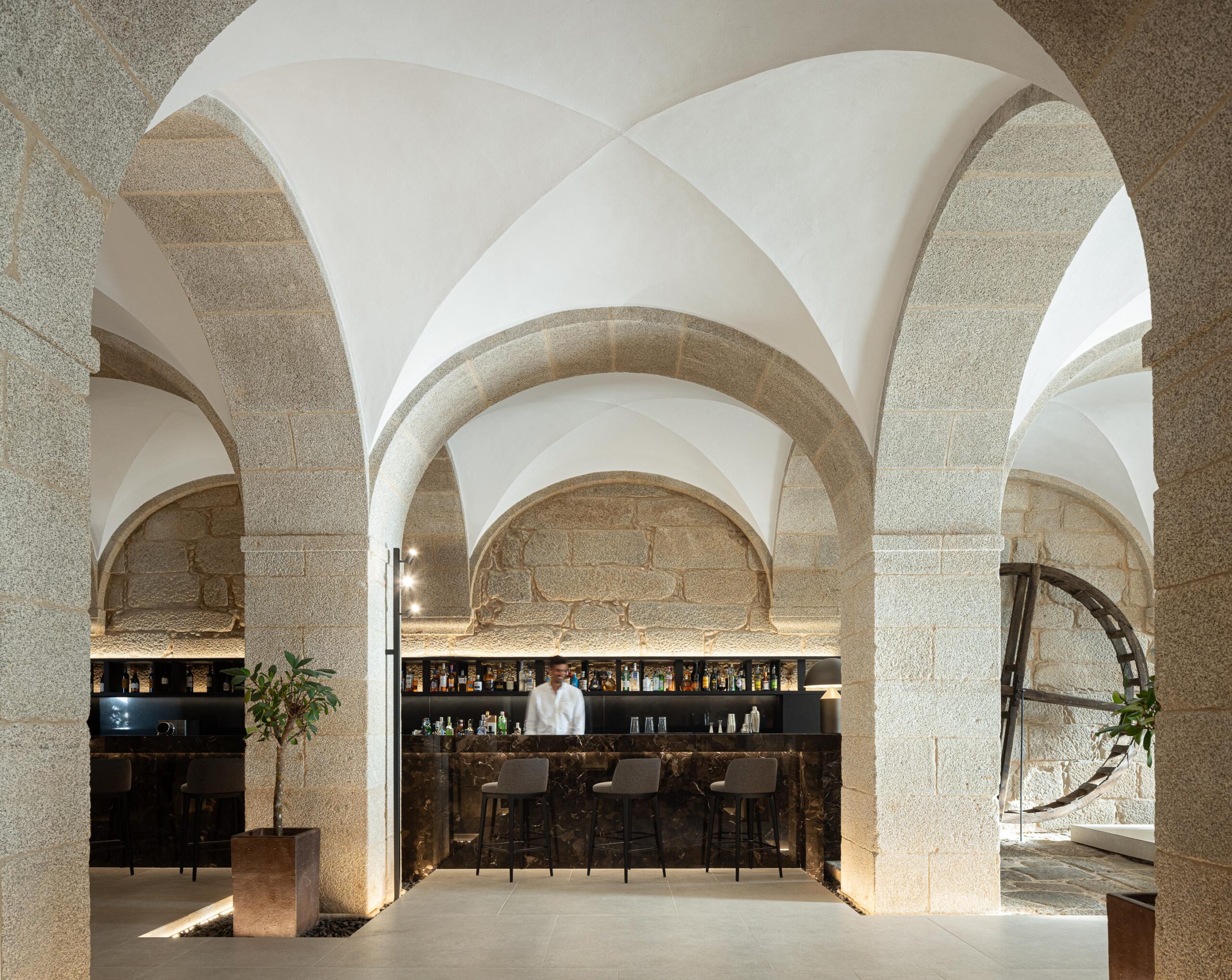 Interior do bar com balcão em mármore escuro, arcos de pedra e abóbadas brancas, criando uma atmosfera de recolhimento — MS COLLECTION AROUCA arquitectura MIMOOL ARQUITECTURA & INTERIORES fotografia Ivo Tavares