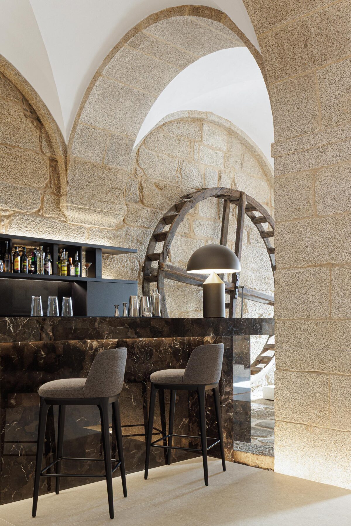 Detalhe do balcão do bar em mármore escuro, com candeeiro de mesa e uma antiga roda de madeira ao fundo — MS COLLECTION AROUCA arquitectura MIMOOL ARQUITECTURA & INTERIORES fotografia Ivo Tavares