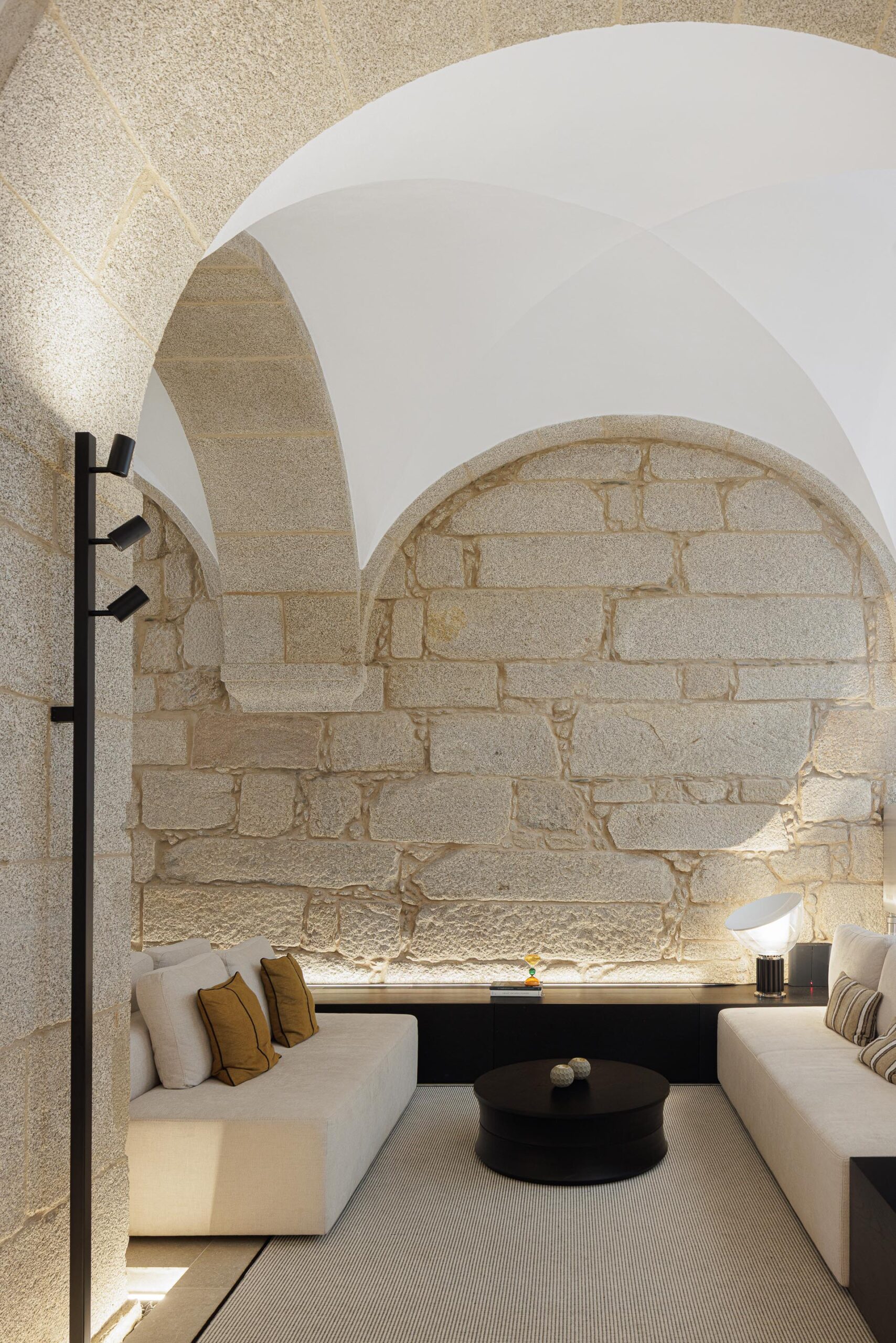 Sala de estar com sofás claros, pavimento em pedra e paredes de alvenaria de pedra, sob arcos e abóbadas — MS COLLECTION AROUCA arquitectura MIMOOL ARQUITECTURA & INTERIORES fotografia Ivo Tavares