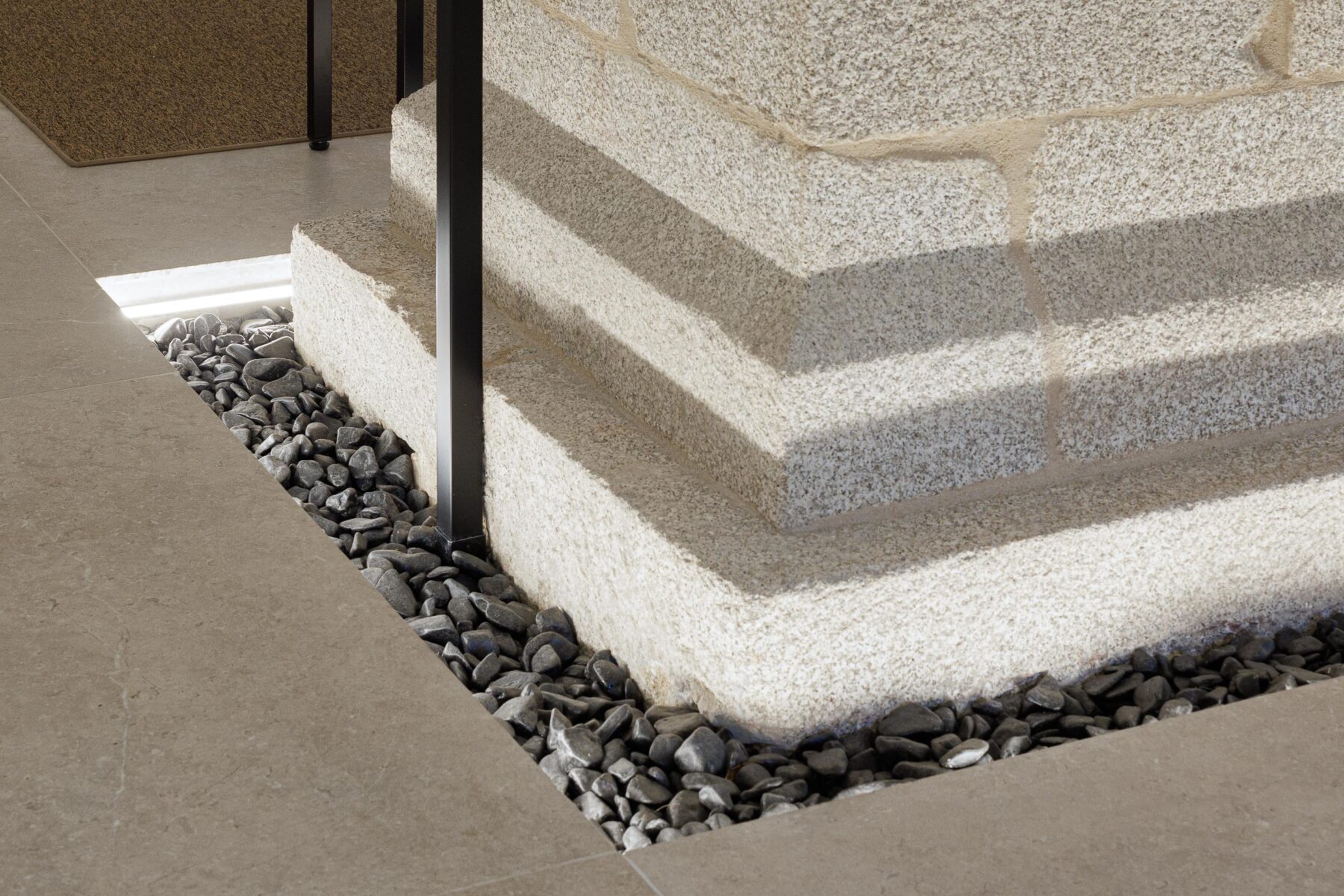 Detalhe da base de uma coluna de pedra, com pavimento em pedra e seixos negros, realçando a materialidade — MS COLLECTION AROUCA arquitectura MIMOOL ARQUITECTURA & INTERIORES fotografia Ivo Tavares