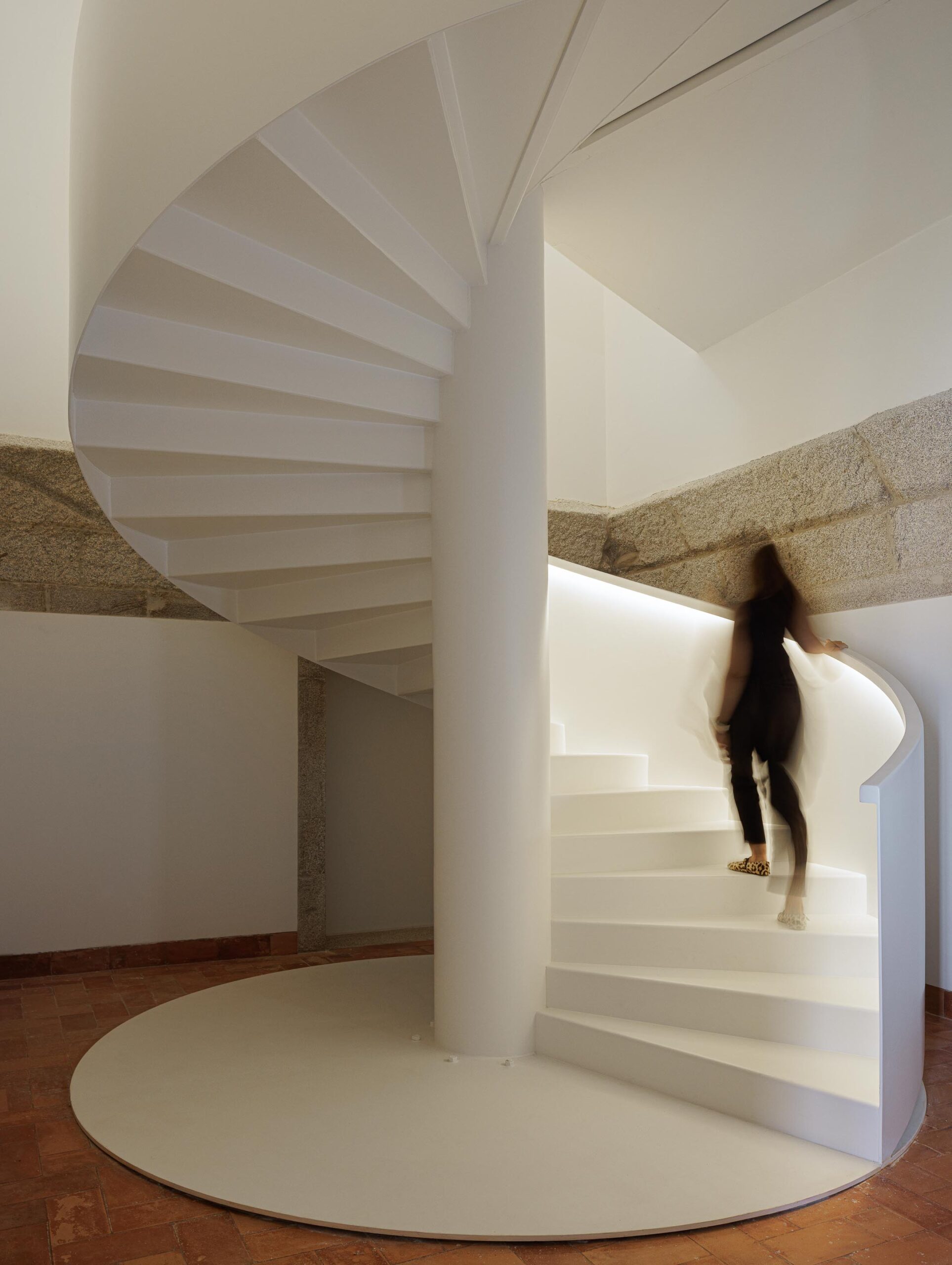 Escadaria em espiral branca, com iluminação linear e pavimento em tijoleira, revelando a estrutura antiga — MS COLLECTION AROUCA arquitectura MIMOOL ARQUITECTURA & INTERIORES fotografia Ivo Tavares