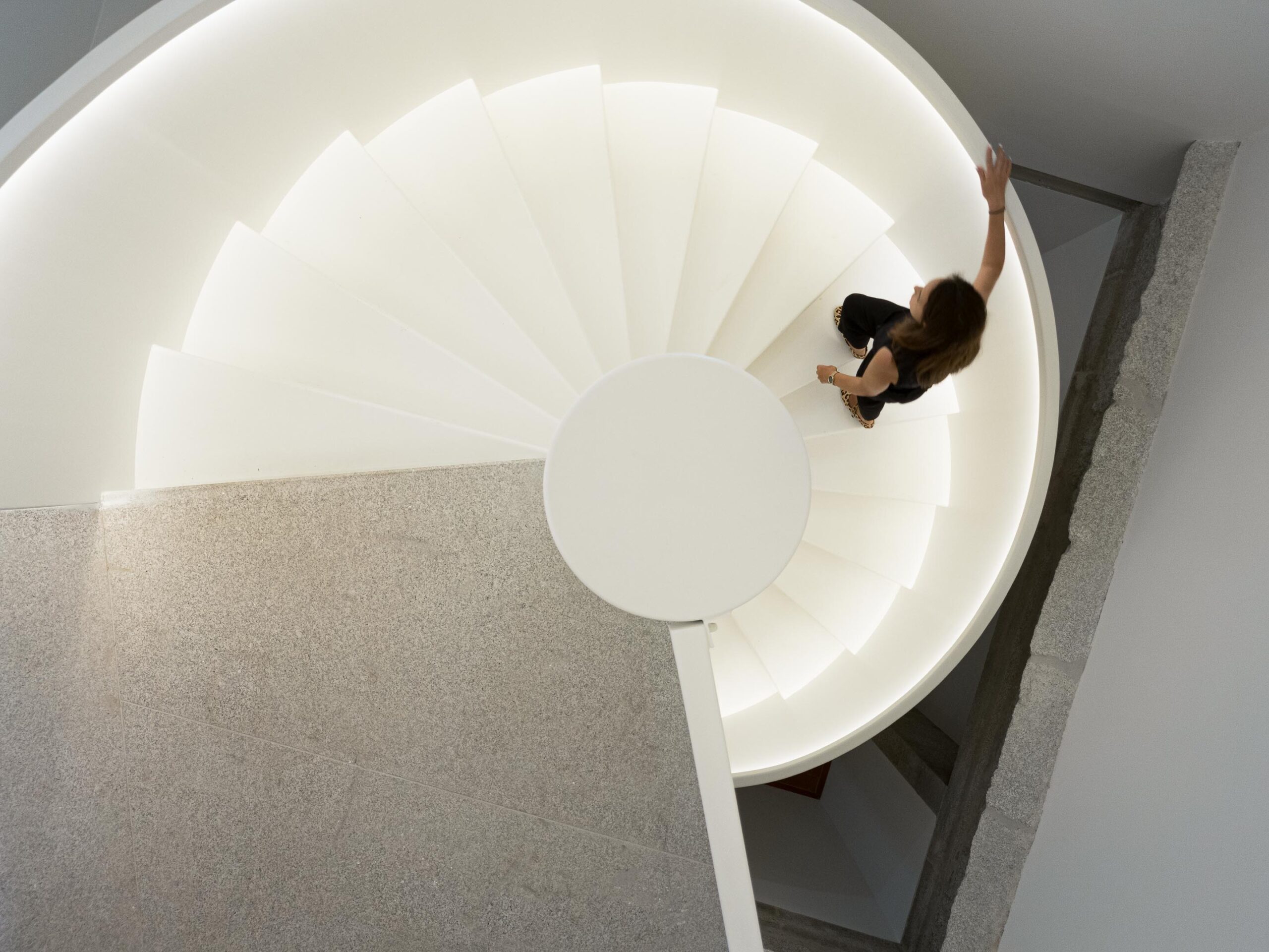 Vista superior da escadaria em espiral branca, com iluminação integrada, ligando diferentes níveis do edifício — MS COLLECTION AROUCA arquitectura MIMOOL ARQUITECTURA & INTERIORES fotografia Ivo Tavares