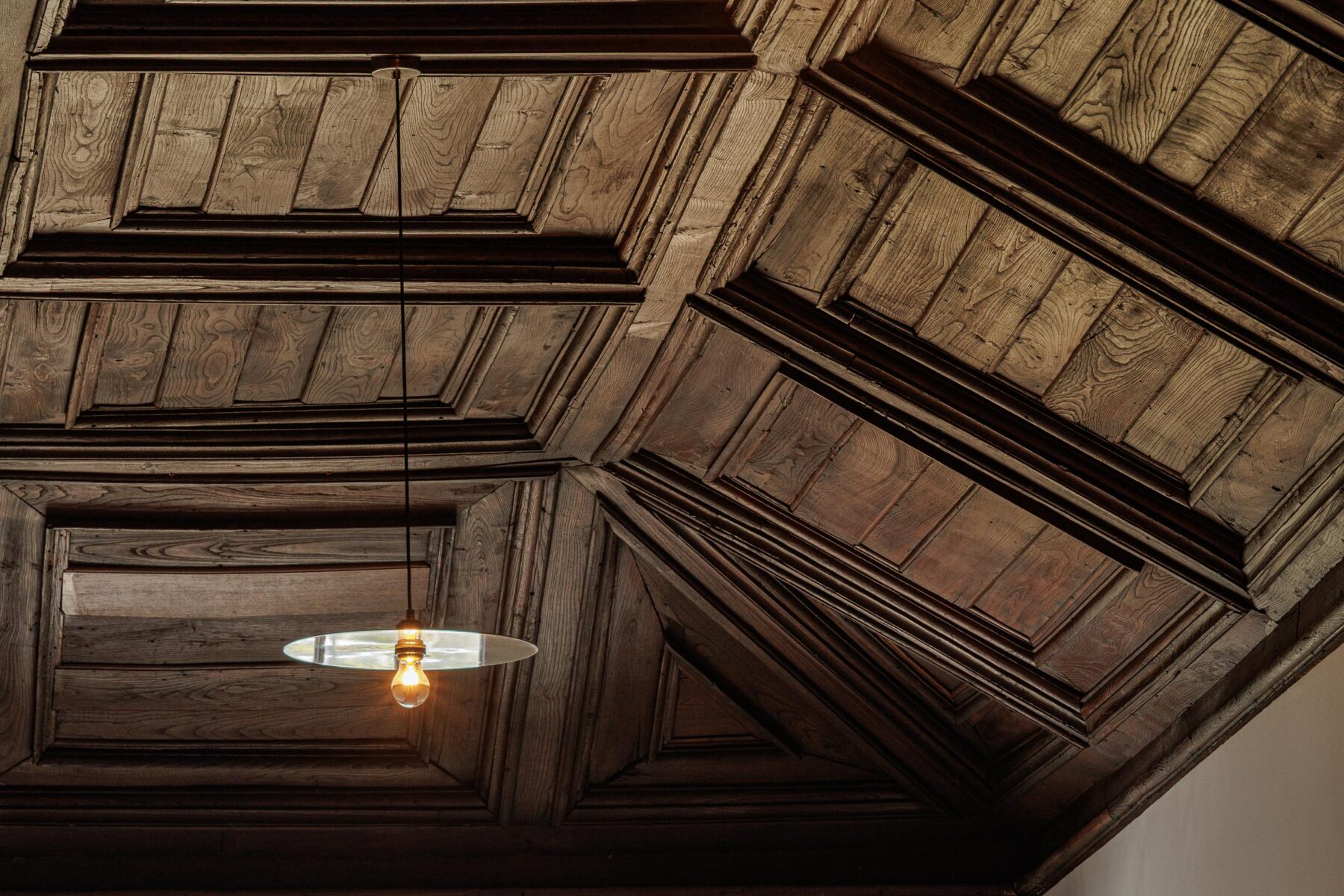 Teto em madeira escura trabalhada, com candeeiro suspenso, revelando a riqueza dos detalhes históricos — MS COLLECTION AROUCA arquitectura MIMOOL ARQUITECTURA & INTERIORES fotografia Ivo Tavares