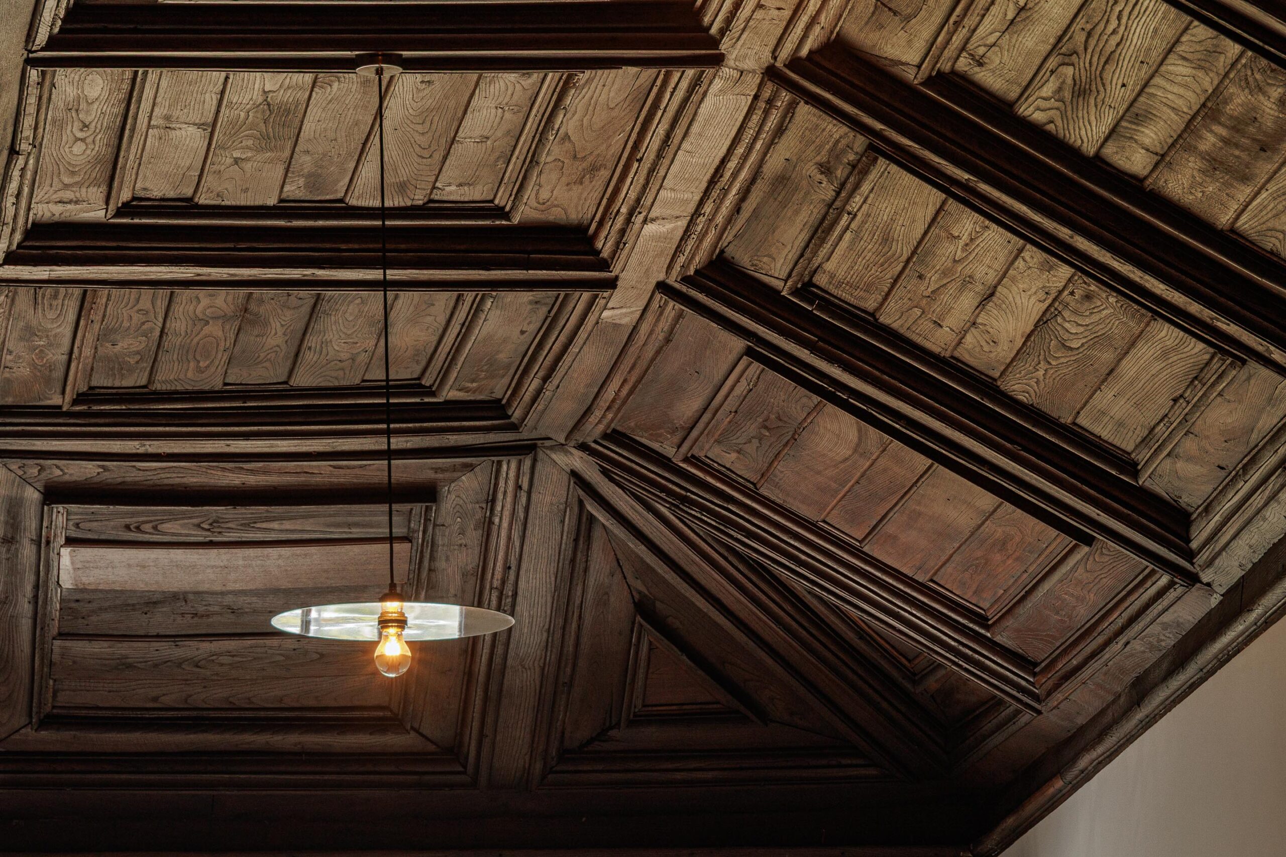 Teto em madeira escura trabalhada, com candeeiro suspenso, revelando a riqueza dos detalhes históricos — MS COLLECTION AROUCA arquitectura MIMOOL ARQUITECTURA & INTERIORES fotografia Ivo Tavares