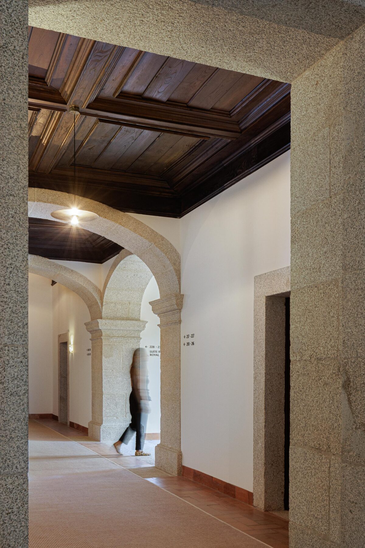Corredor com arcos de pedra e teto em madeira escura, pavimento em tijoleira e tapete, com iluminação discreta — MS COLLECTION AROUCA arquitectura MIMOOL ARQUITECTURA & INTERIORES fotografia Ivo Tavares