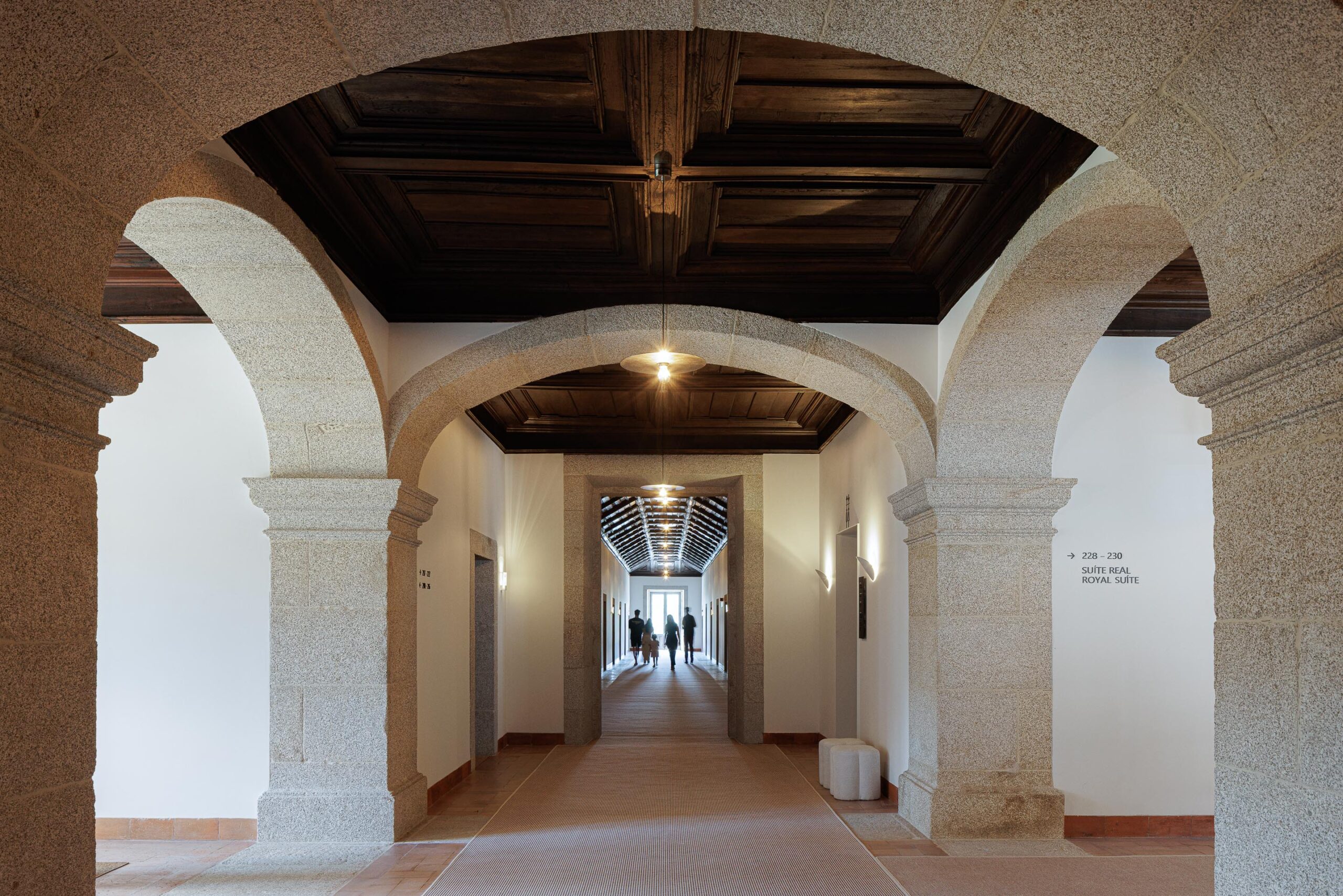 Corredor com arcos de pedra e teto em madeira escura, pavimento em tijoleira e tapete, com iluminação discreta — MS COLLECTION AROUCA arquitectura MIMOOL ARQUITECTURA & INTERIORES fotografia Ivo Tavares