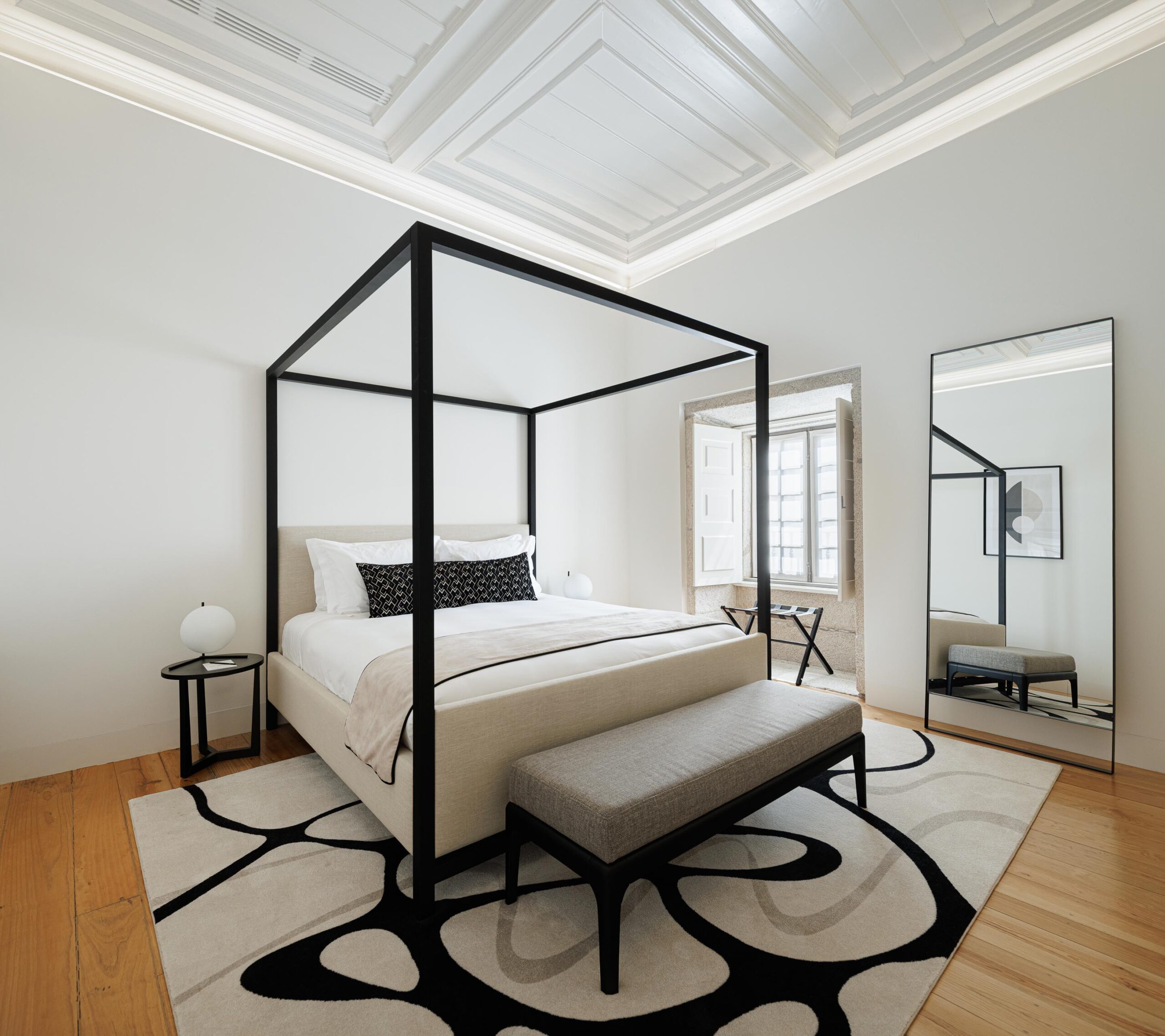 Quarto com cama de dossel em metal negro, pavimento em madeira clara e teto branco trabalhado, com janela em pedra — MS COLLECTION AROUCA arquitectura MIMOOL ARQUITECTURA & INTERIORES fotografia Ivo Tavares