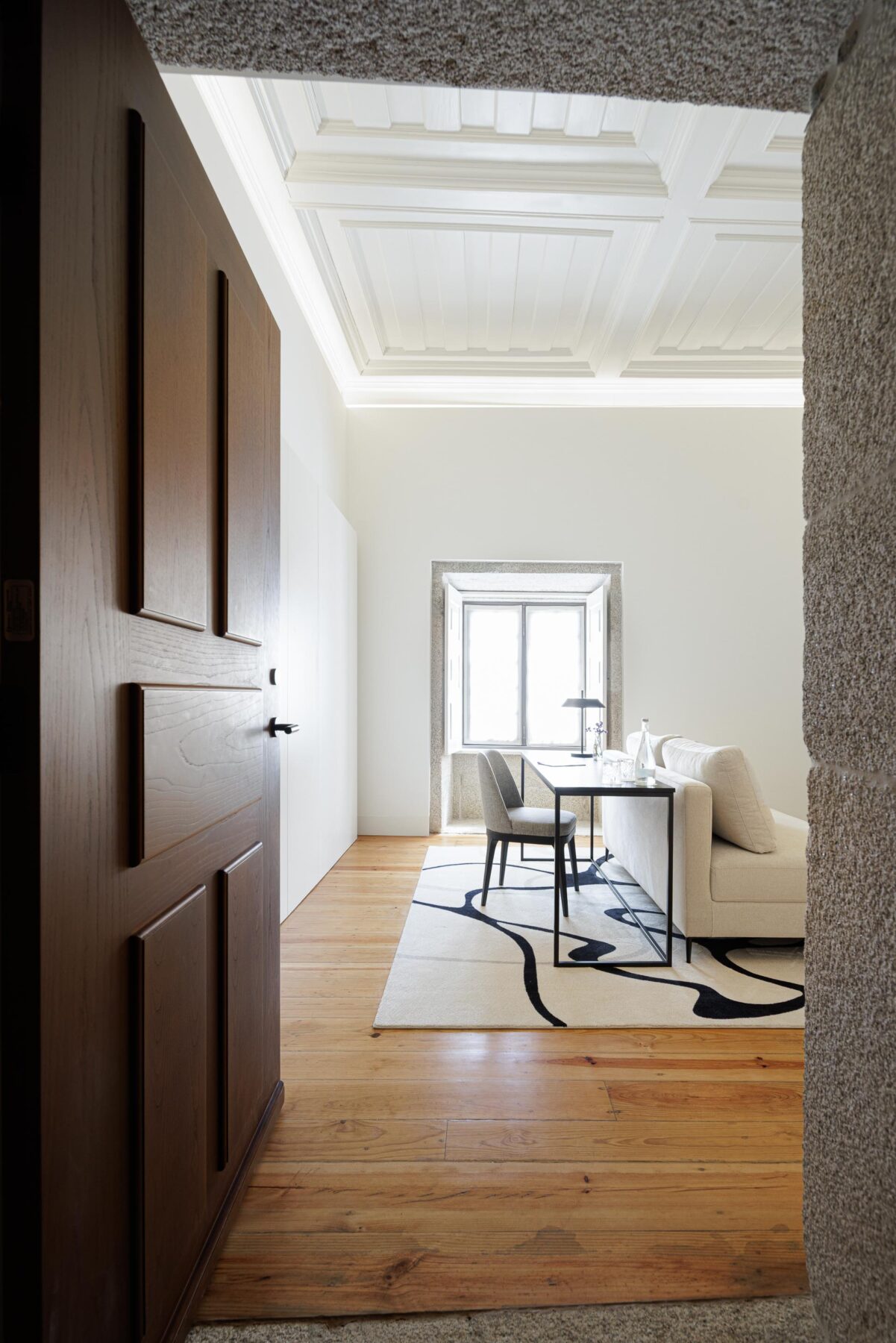 Interior do quarto com pavimento em madeira clara, teto branco trabalhado e janela em pedra, com secretária e sofá — MS COLLECTION AROUCA arquitectura MIMOOL ARQUITECTURA & INTERIORES fotografia Ivo Tavares