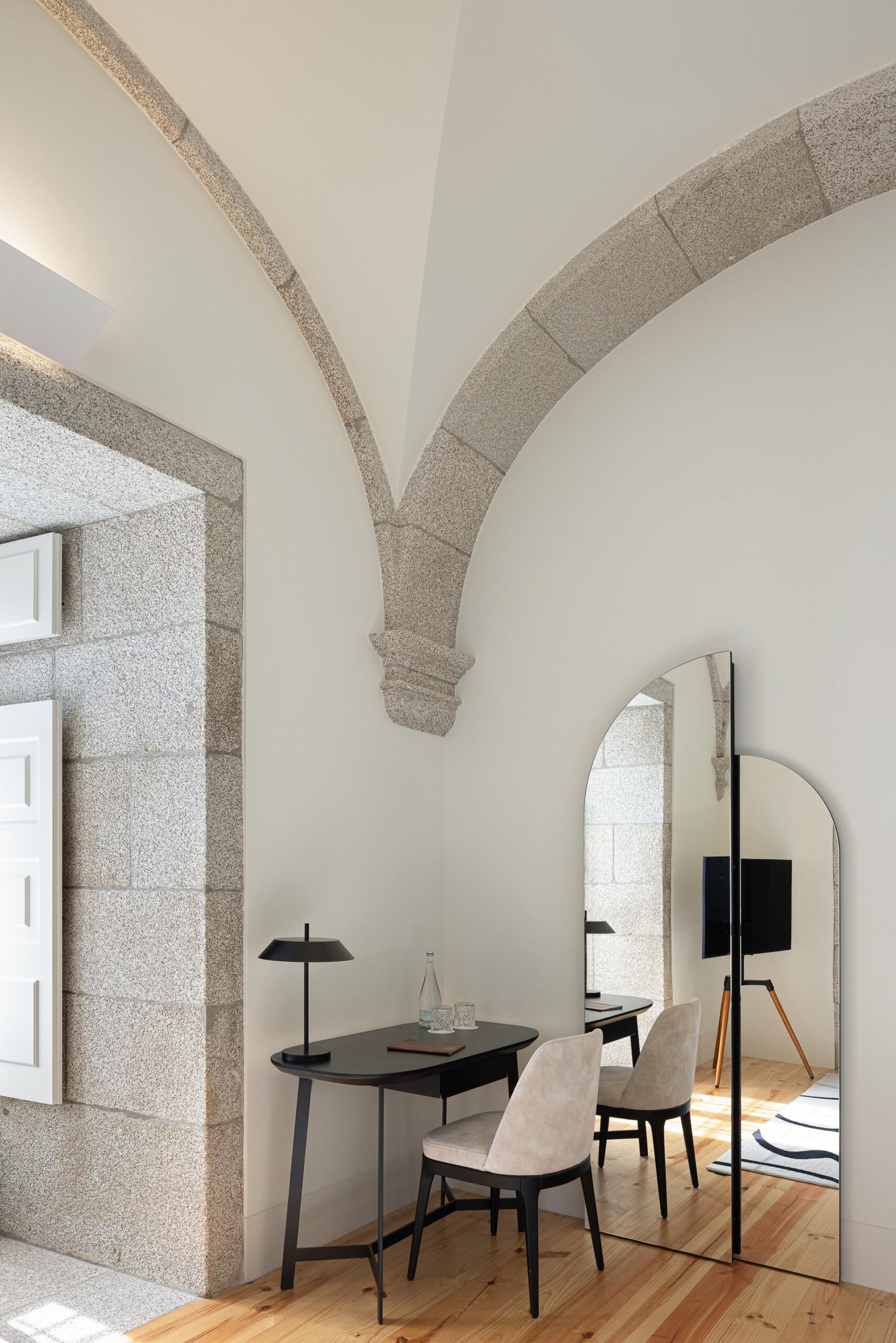 Quarto com secretária, pavimento em madeira clara, abóbadas de pedra e espelho em arco, com vista para a casa de banho — MS COLLECTION AROUCA arquitectura MIMOOL ARQUITECTURA & INTERIORES fotografia Ivo Tavares