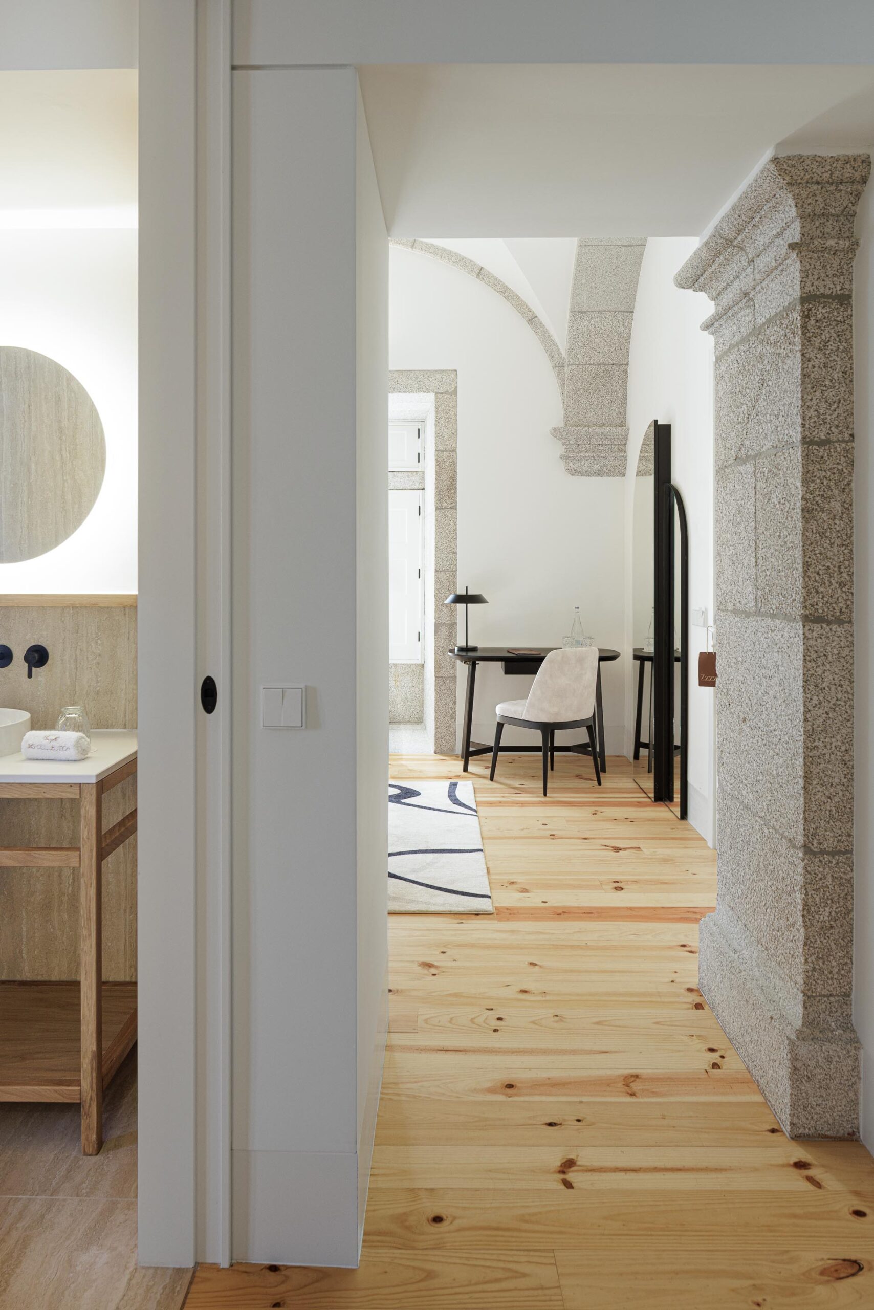 Casa de banho com lavatórios duplos, espelho iluminado e revestimento em pedra clara, com vista para o quarto — MS COLLECTION AROUCA arquitectura MIMOOL ARQUITECTURA & INTERIORES fotografia Ivo Tavares