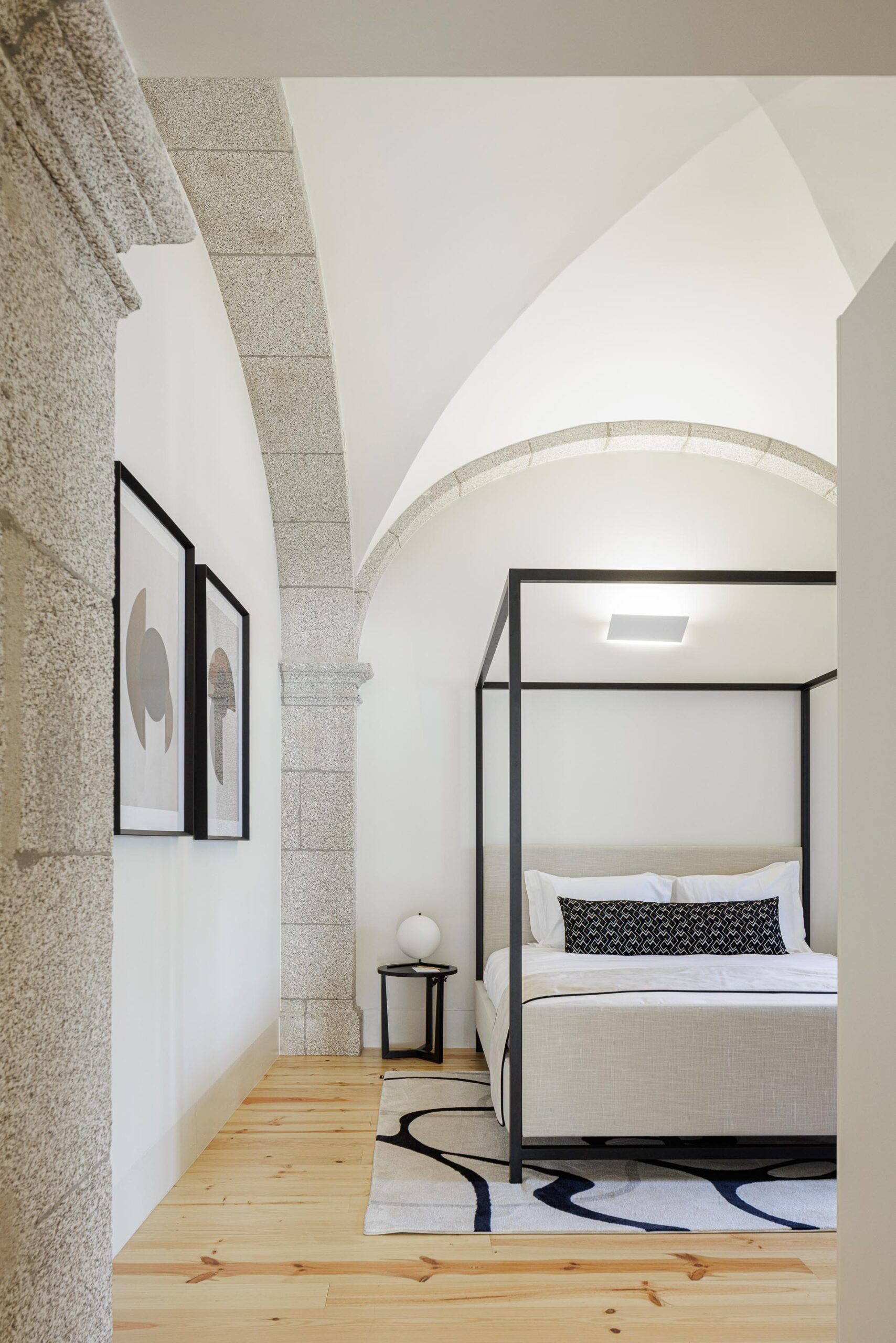 Quarto com cama de dossel preta, pavimento em madeira clara e arco em pedra, com quadros na parede — MS COLLECTION AROUCA arquitectura MIMOOL ARQUITECTURA & INTERIORES fotografia Ivo Tavares
