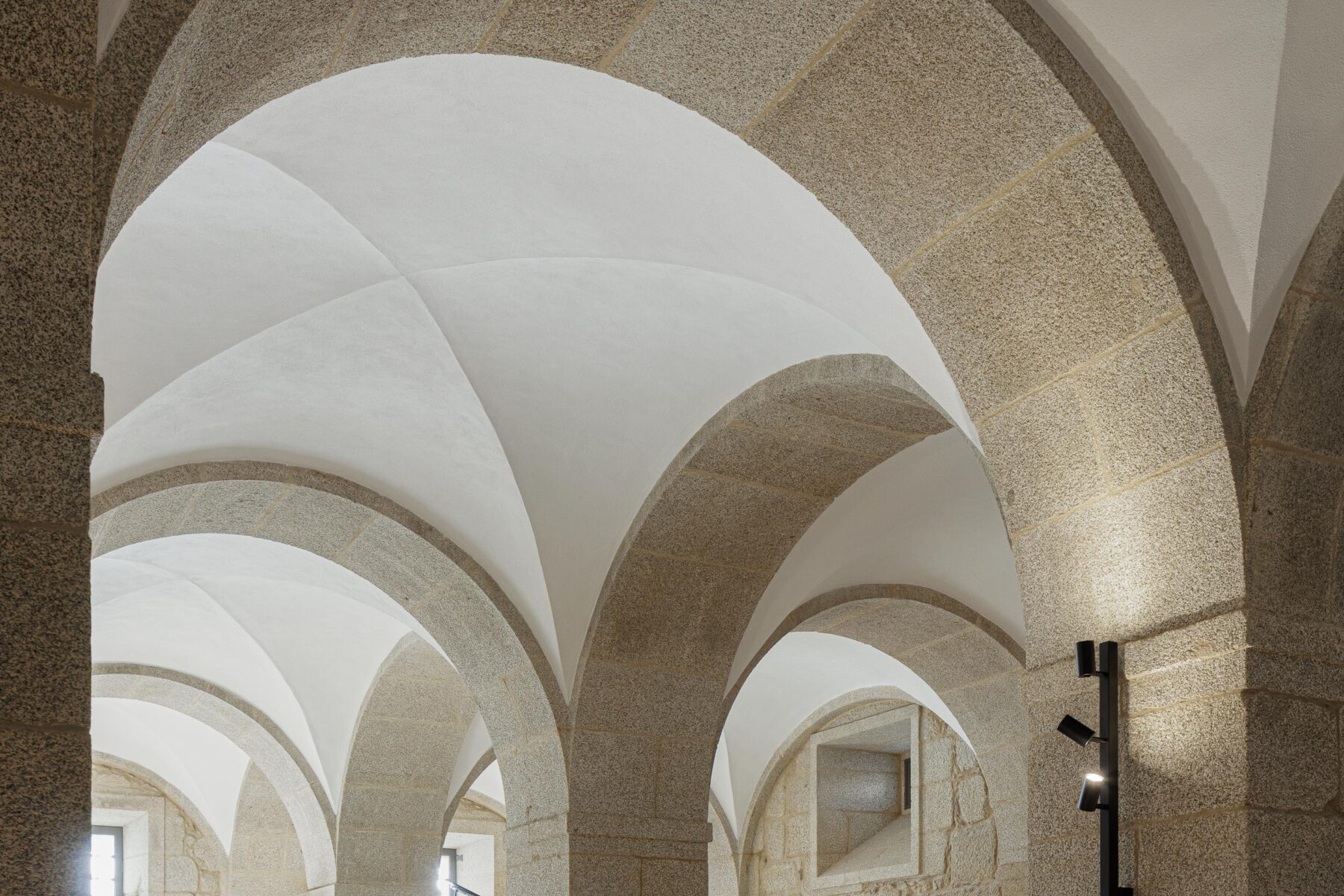 Detalhe de arcos em pedra e abóbadas brancas, com iluminação embutida, criando um jogo de luz e sombra — MS COLLECTION AROUCA arquitectura MIMOOL ARQUITECTURA & INTERIORES fotografia Ivo Tavares
