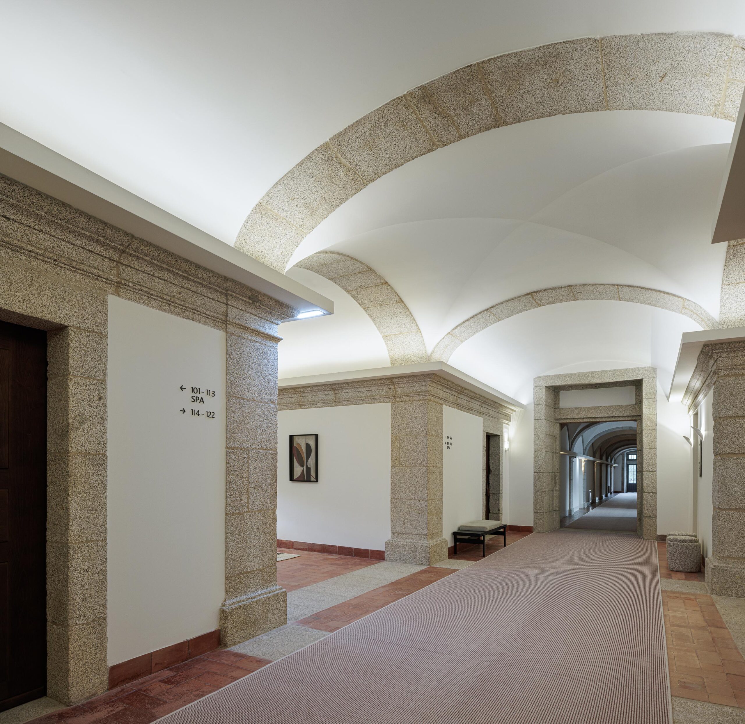Corredor com arcos em pedra, pavimento em tijoleira e tapete, com iluminação de parede e sinalética — MS COLLECTION AROUCA arquitectura MIMOOL ARQUITECTURA & INTERIORES fotografia Ivo Tavares