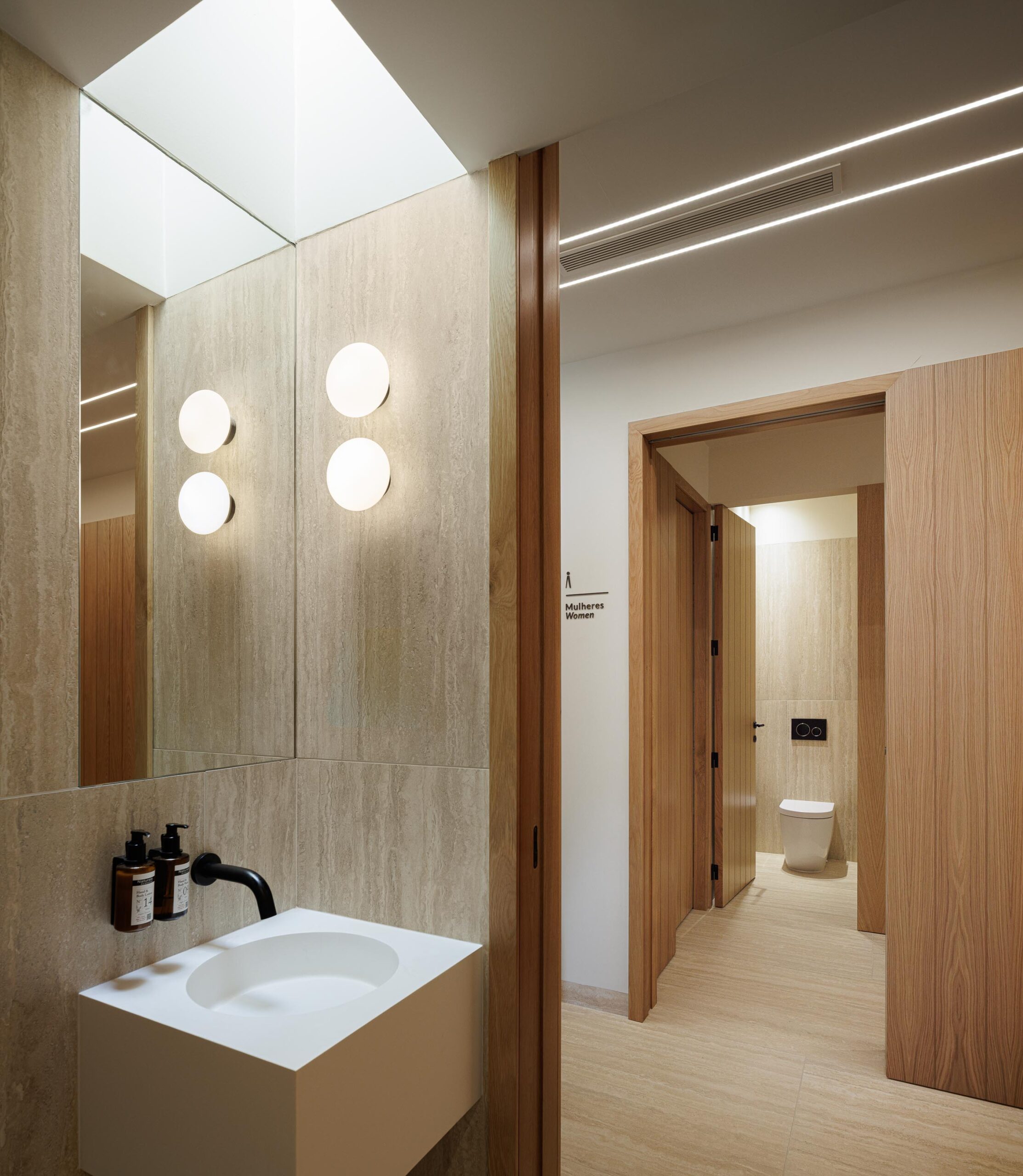 Casa de banho com lavatório branco, espelho e paredes em pedra clara, com porta em madeira — MS COLLECTION AROUCA arquitectura MIMOOL ARQUITECTURA & INTERIORES fotografia Ivo Tavares