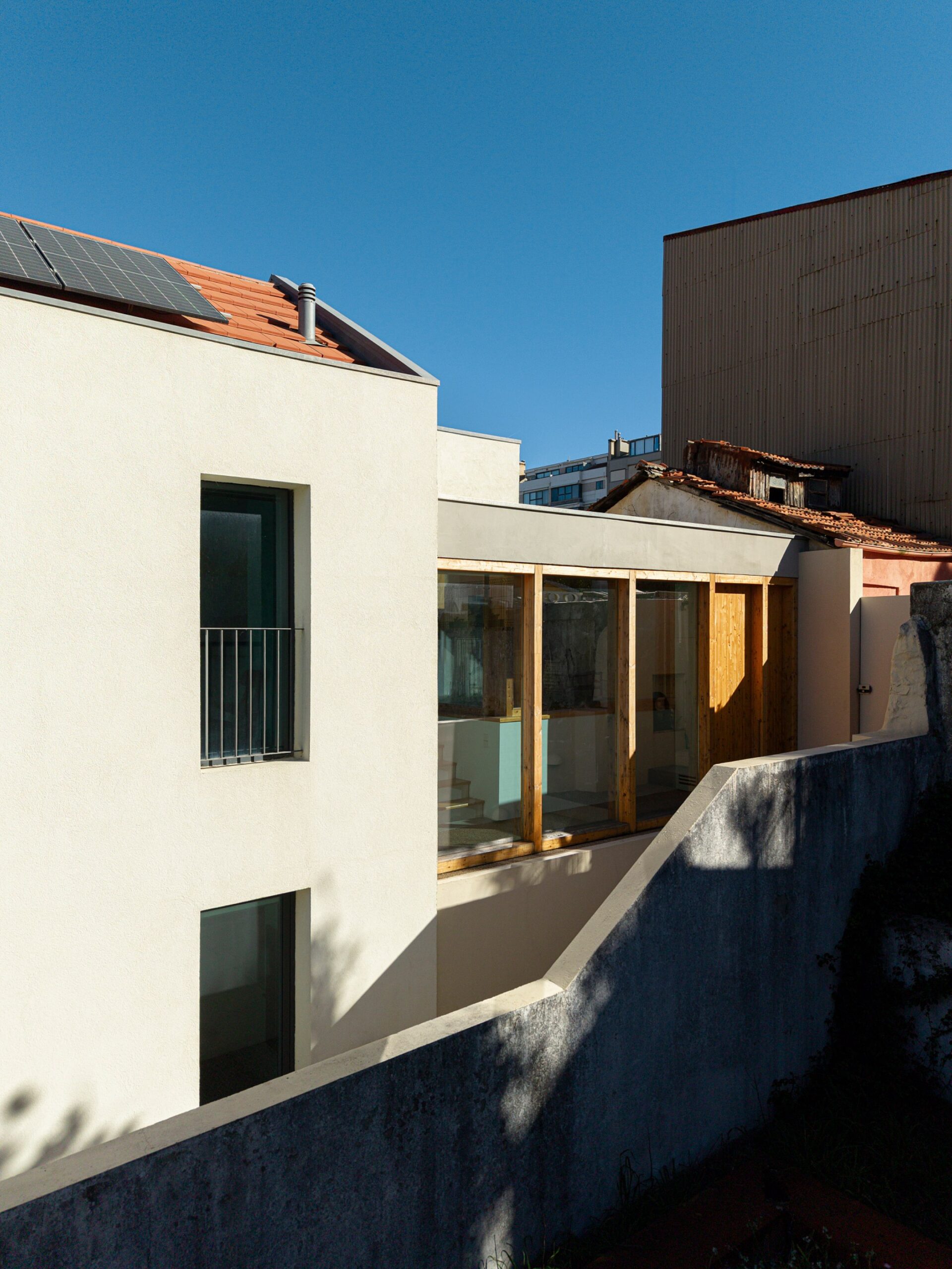 Fachada lateral da moradia com revestimento branco, vãos verticais e passadiço envidraçado em madeira — Casa sem Rua