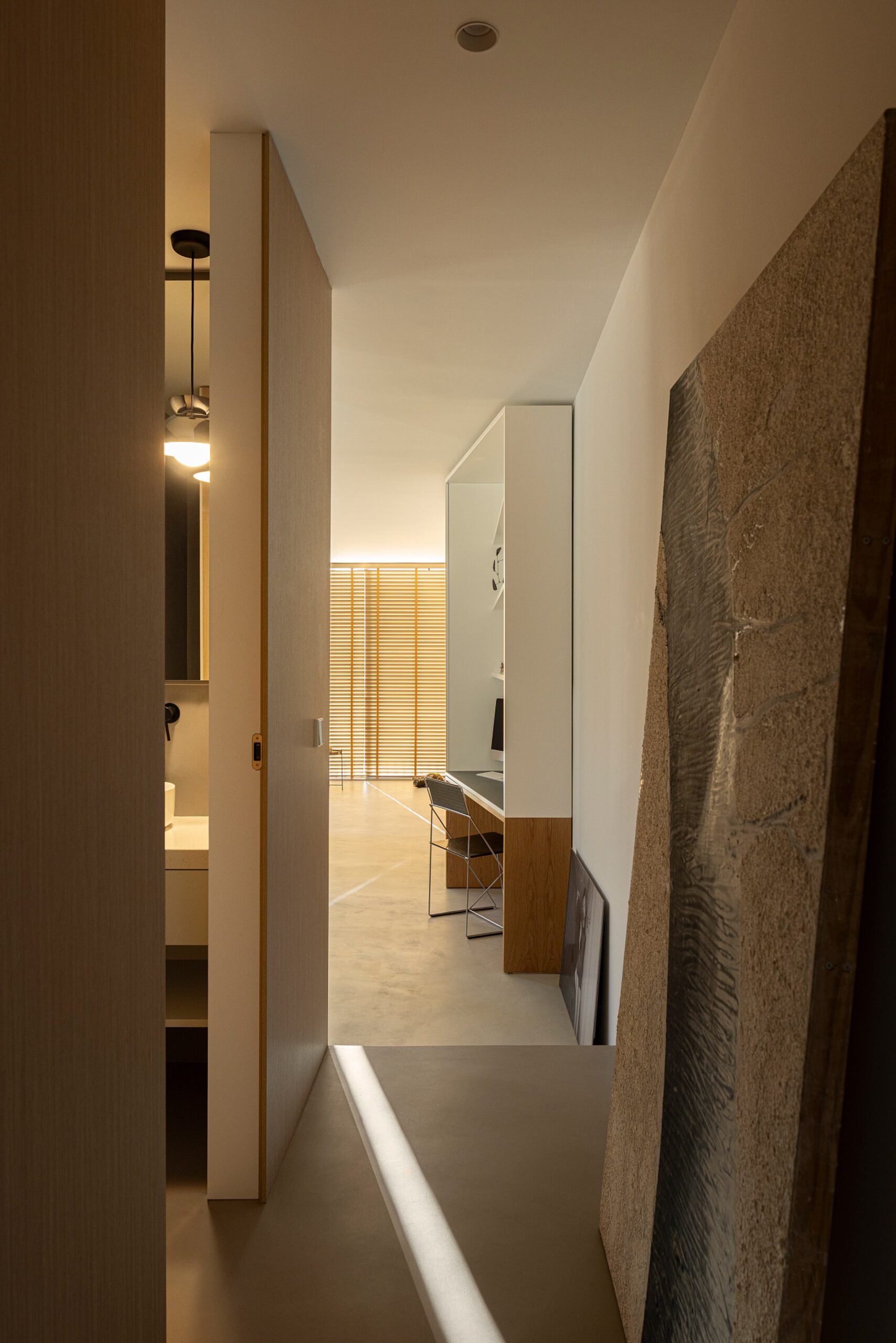 Corredor interior com pavimento cinzento, porta em madeira clara e vista para um espaço de trabalho — Casa sem Rua