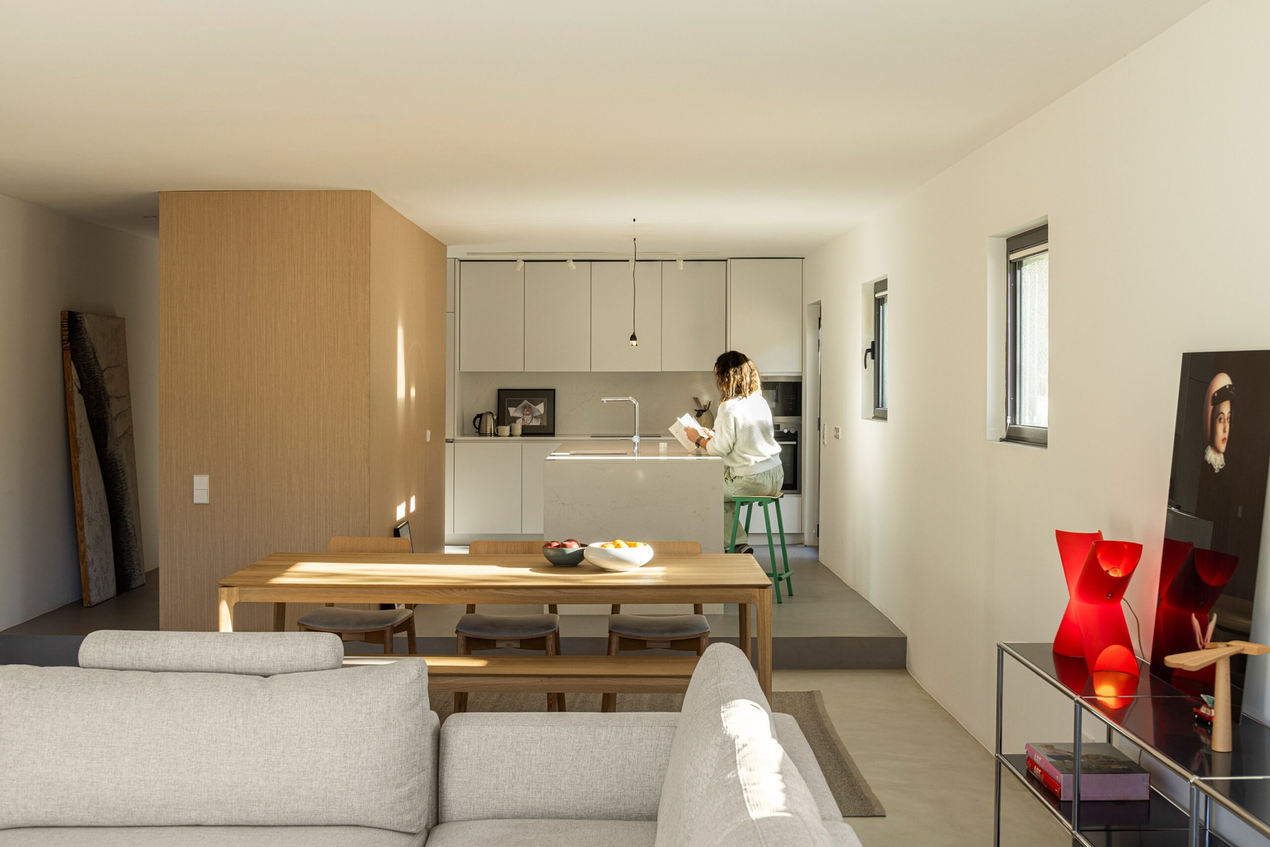 Sala de estar e jantar em plano aberto, com pavimento cinzento, mesa de madeira e sofá cinzento — Casa sem Rua