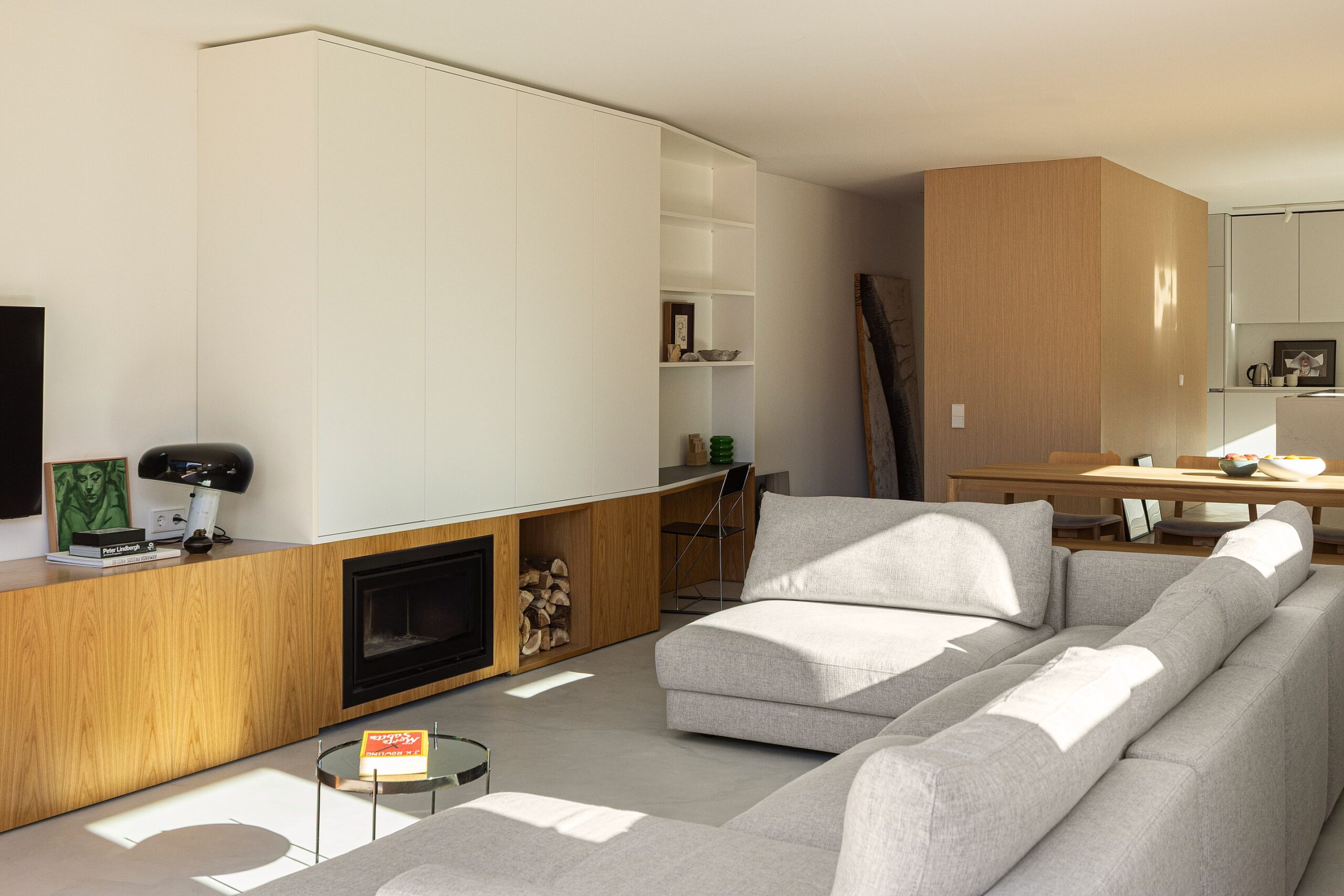 Sala de estar com sofá cinzento, pavimento cinzento, lareira e armários em madeira clara e branco — Casa sem Rua
