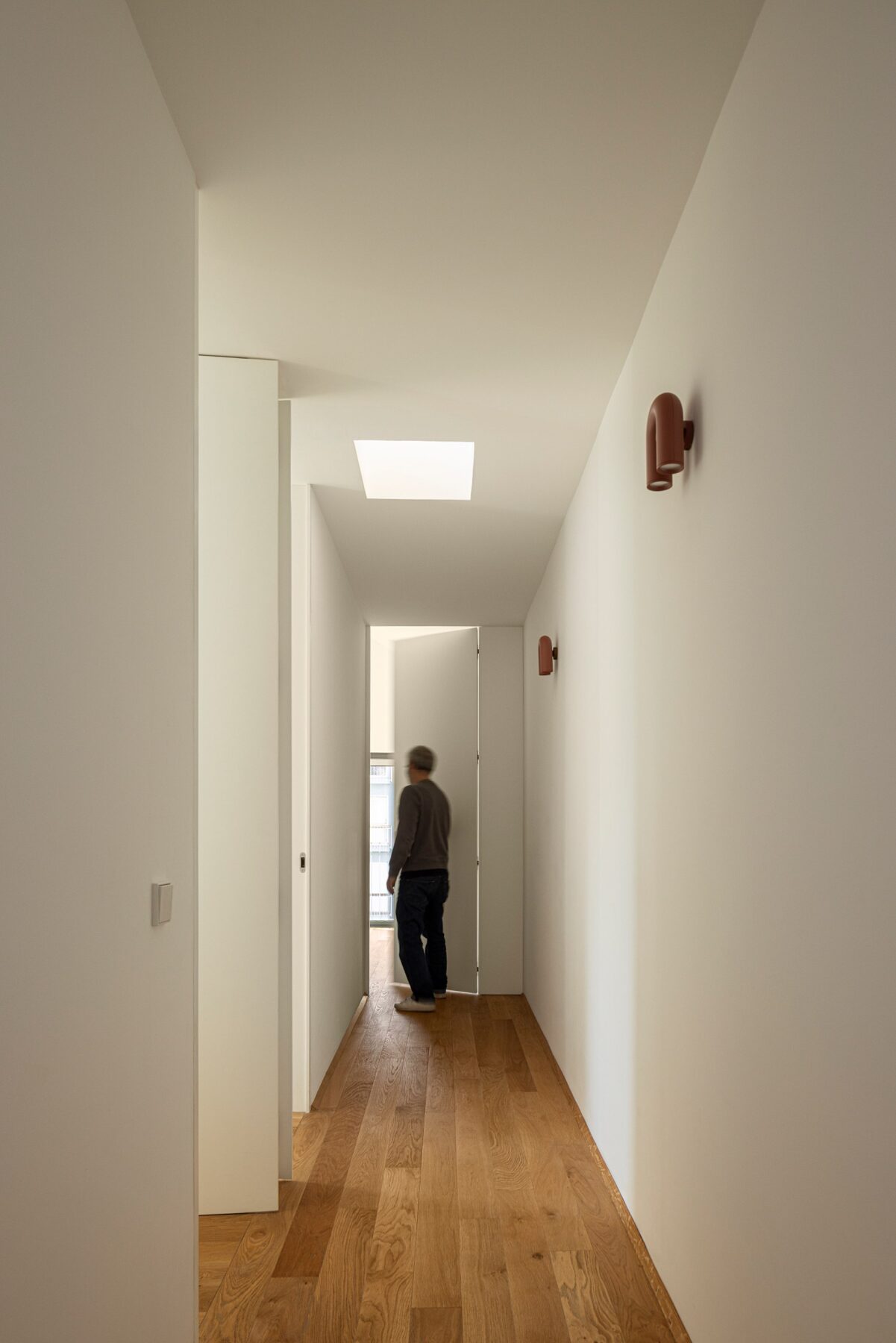 Corredor interior com pavimento em madeira de carvalho, iluminação zenital e candeeiros de parede — Casa sem Rua