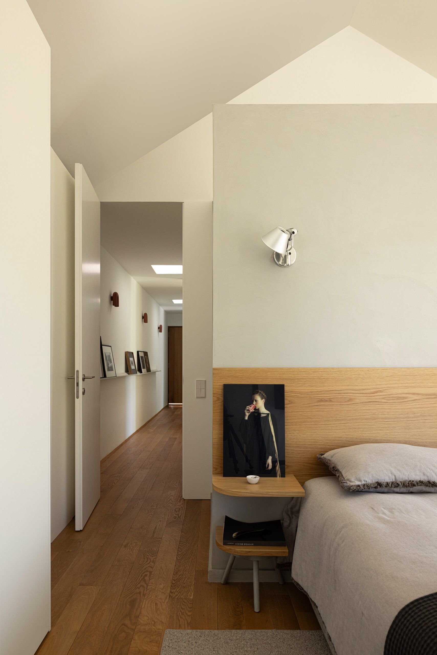 Quarto com pavimento em madeira de carvalho, cabeceira em madeira e parede cinzenta, com corredor ao fundo — Casa sem Rua