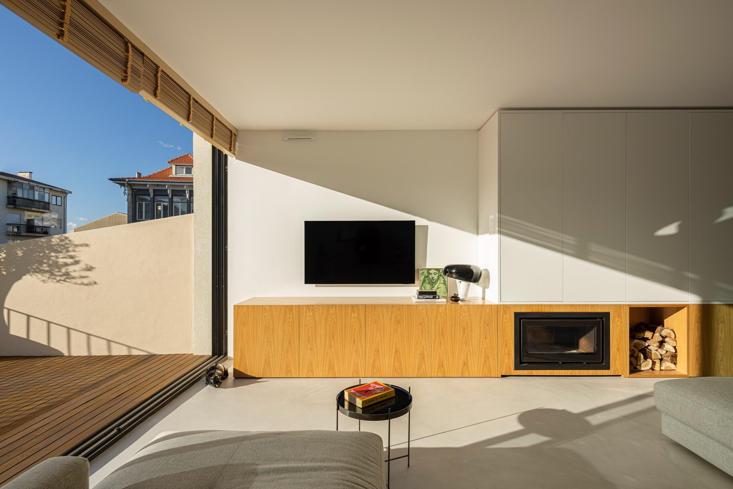Sala de estar com pavimento cinzento, móvel em madeira clara, lareira e vão de correr — Casa sem Rua