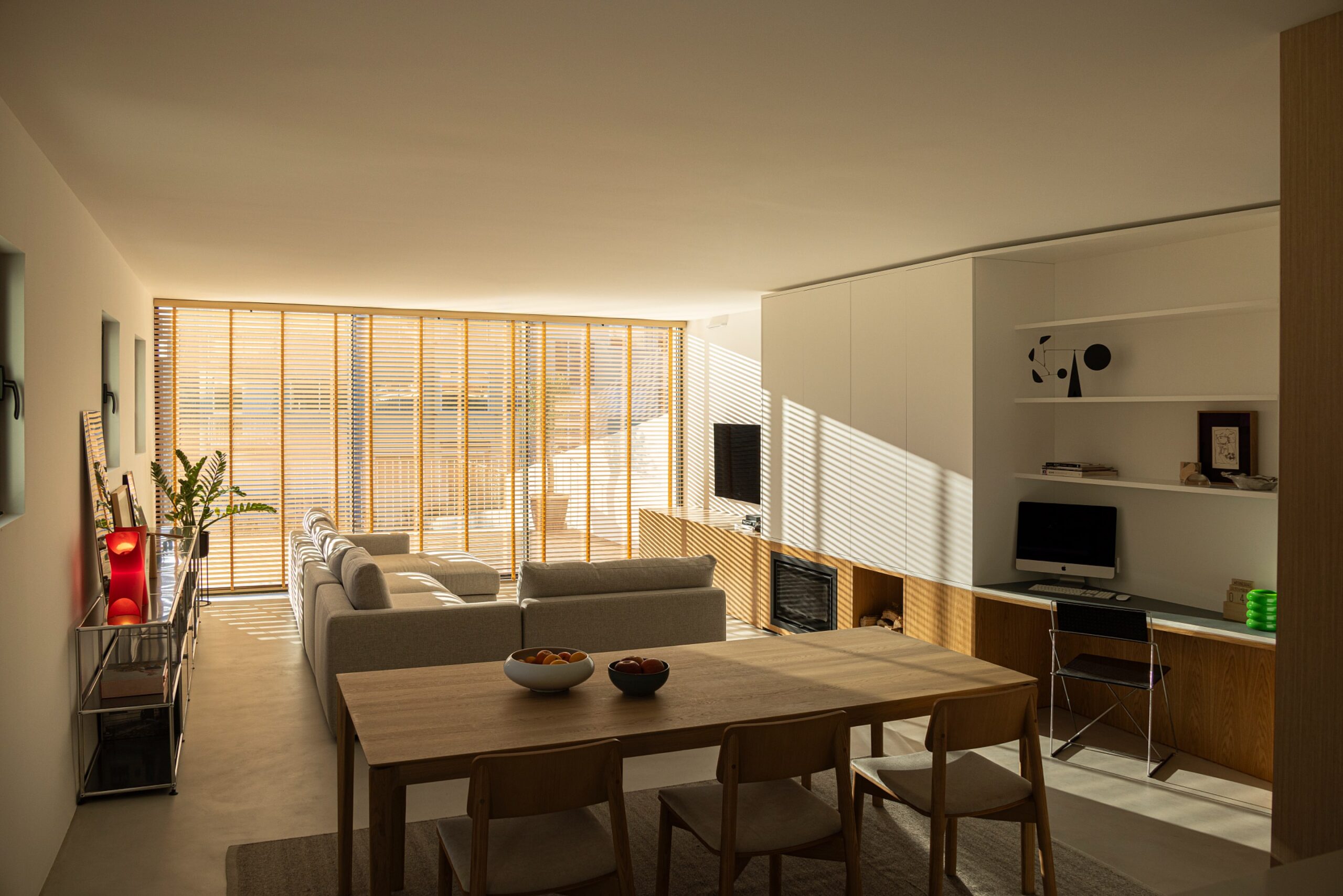 Sala de estar e jantar com luz natural filtrada por estores de madeira, criando padrões de luz — Casa sem Rua